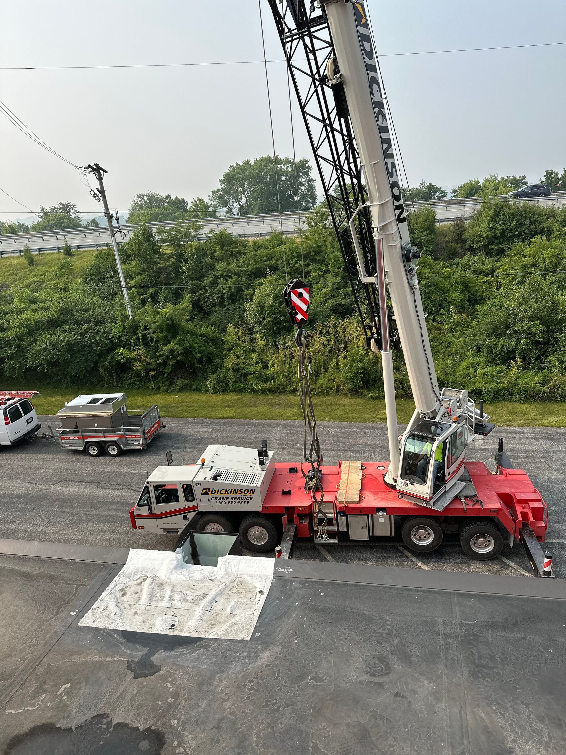 Large crane lifting an object, possibly a transformer. Red and white vehicle on asphalt.