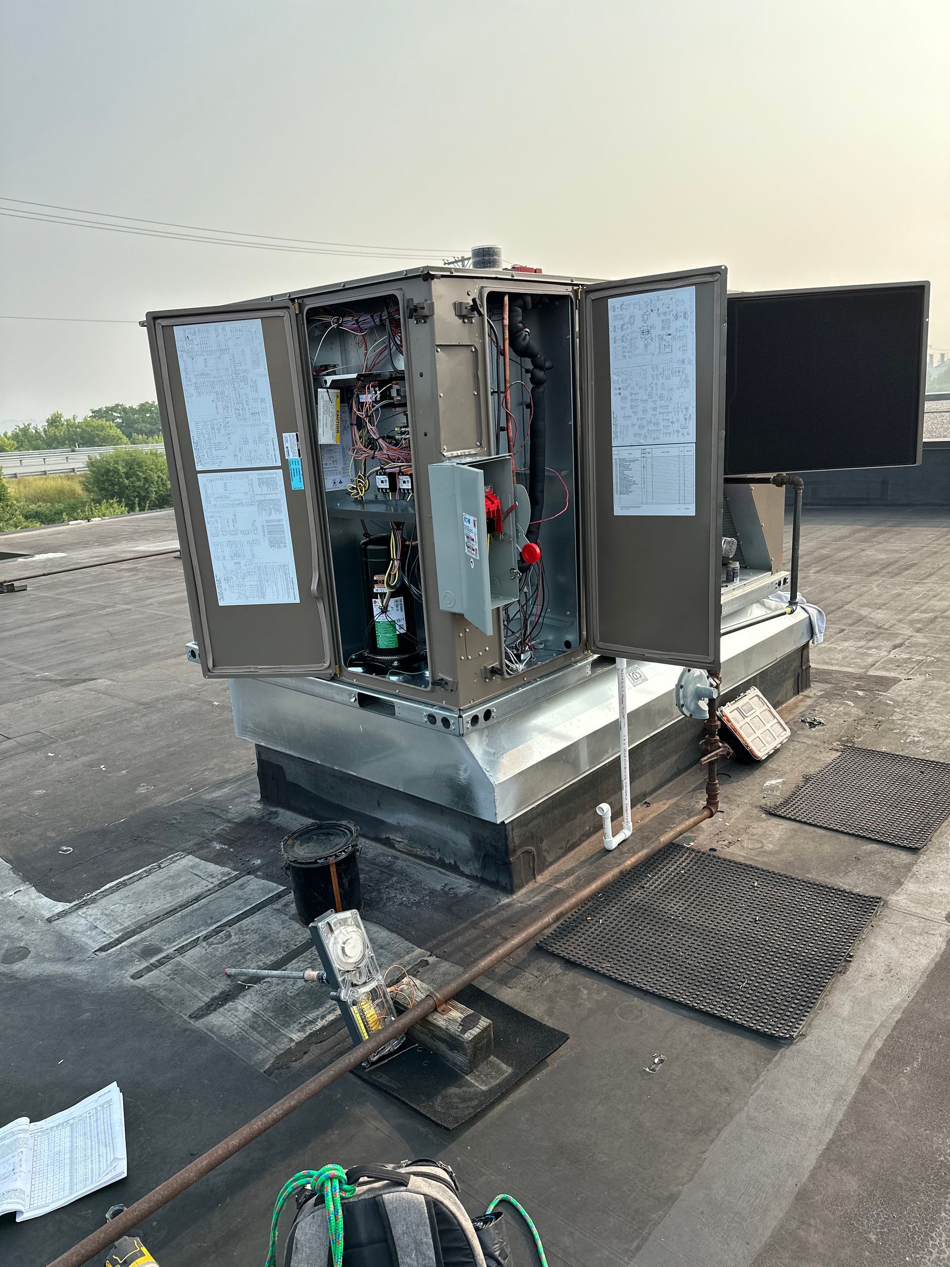 Rooftop HVAC unit with open panels for maintenance, on a flat roof.