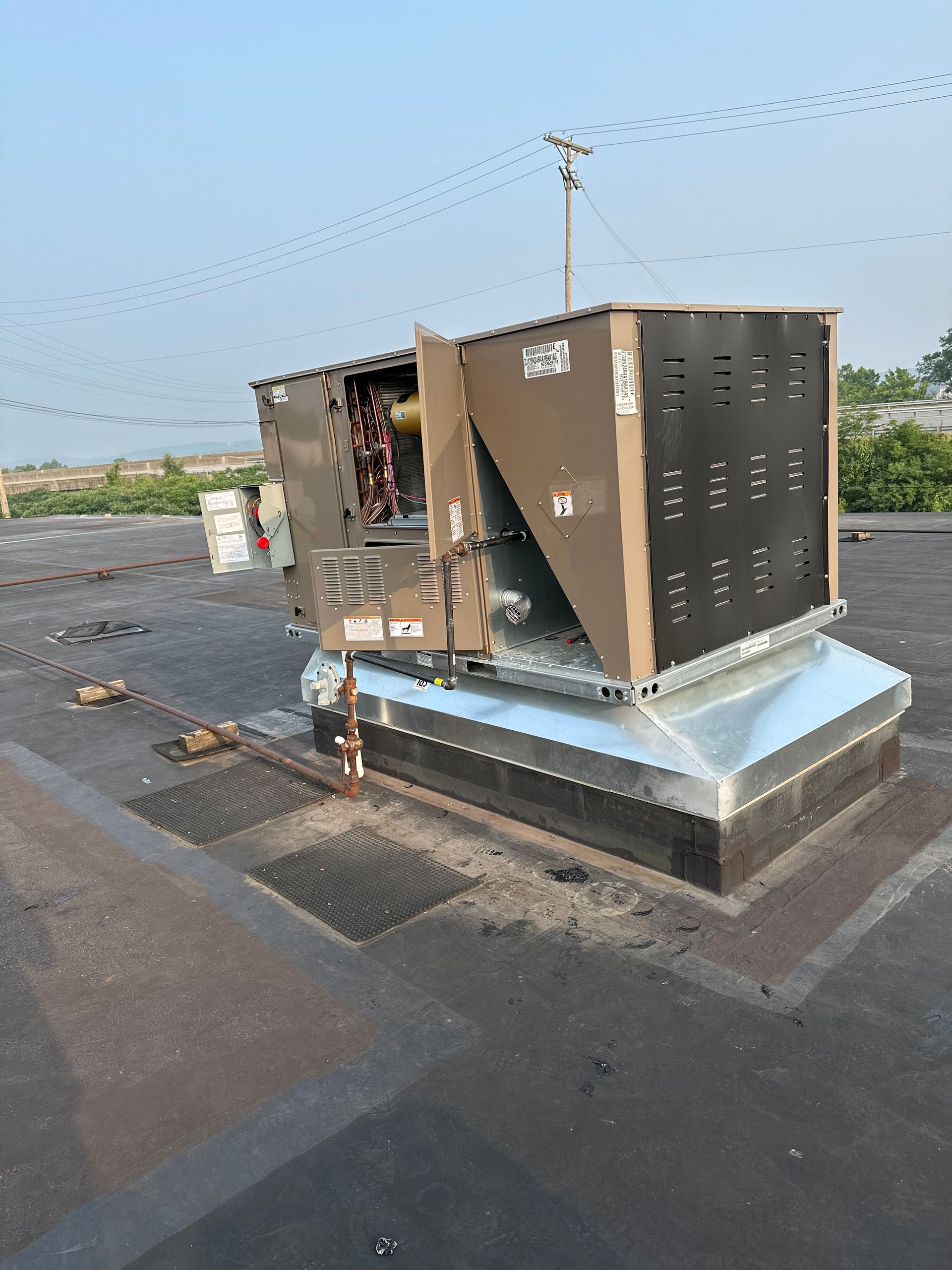 Rooftop HVAC unit with open panels, on a flat tar roof under a blue sky.