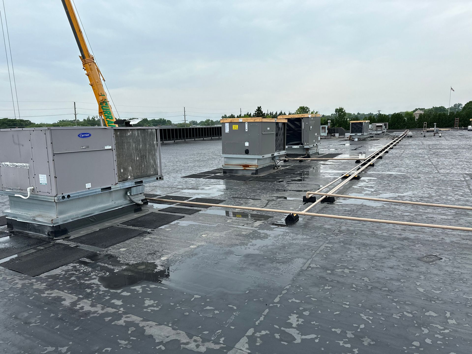 HVAC units on a wet rooftop with a crane arm, cloudy sky.