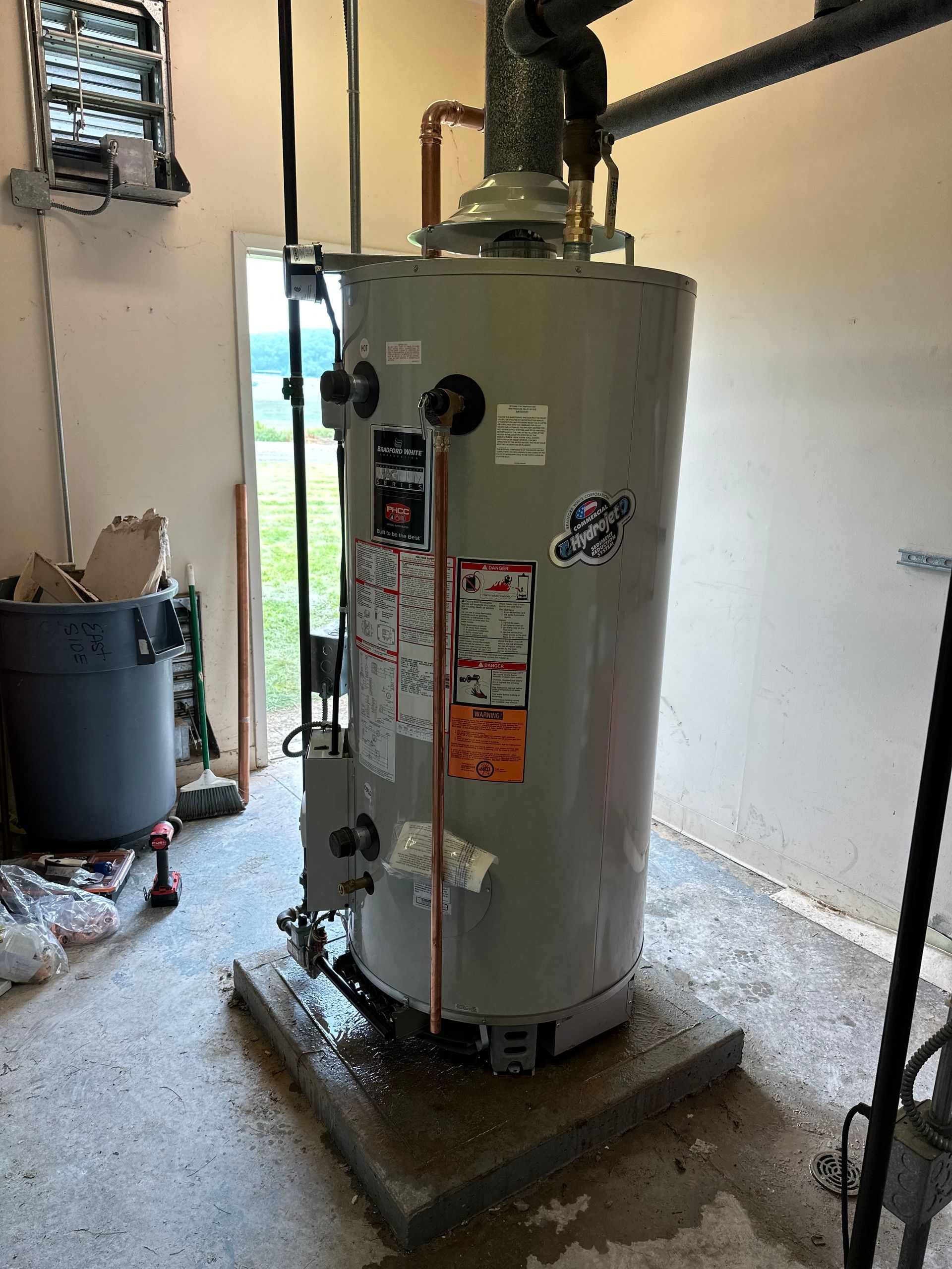 A tall, cylindrical water heater in a garage, with water visible at the base.