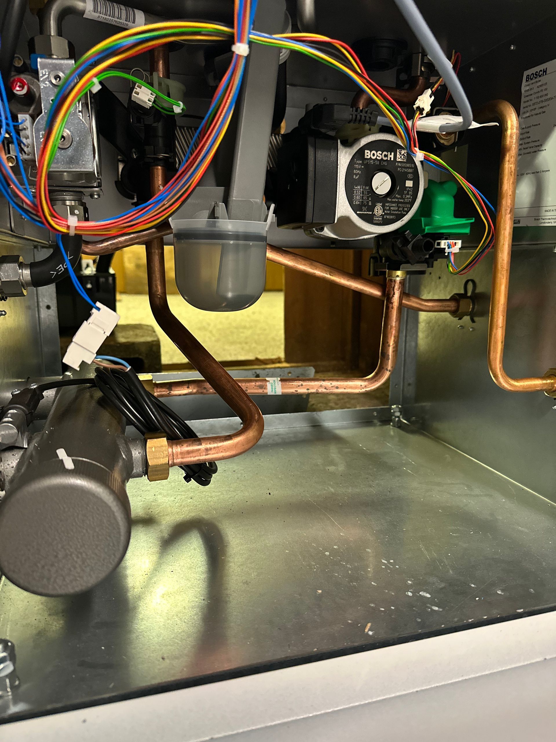 Copper pipes and various components inside a gas boiler, including a pump, valves, and electrical wiring.