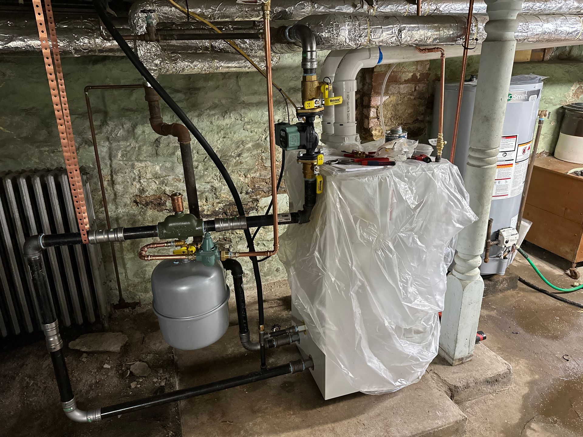 Heating system in a basement, with pipes, a tank, and a covered unit.