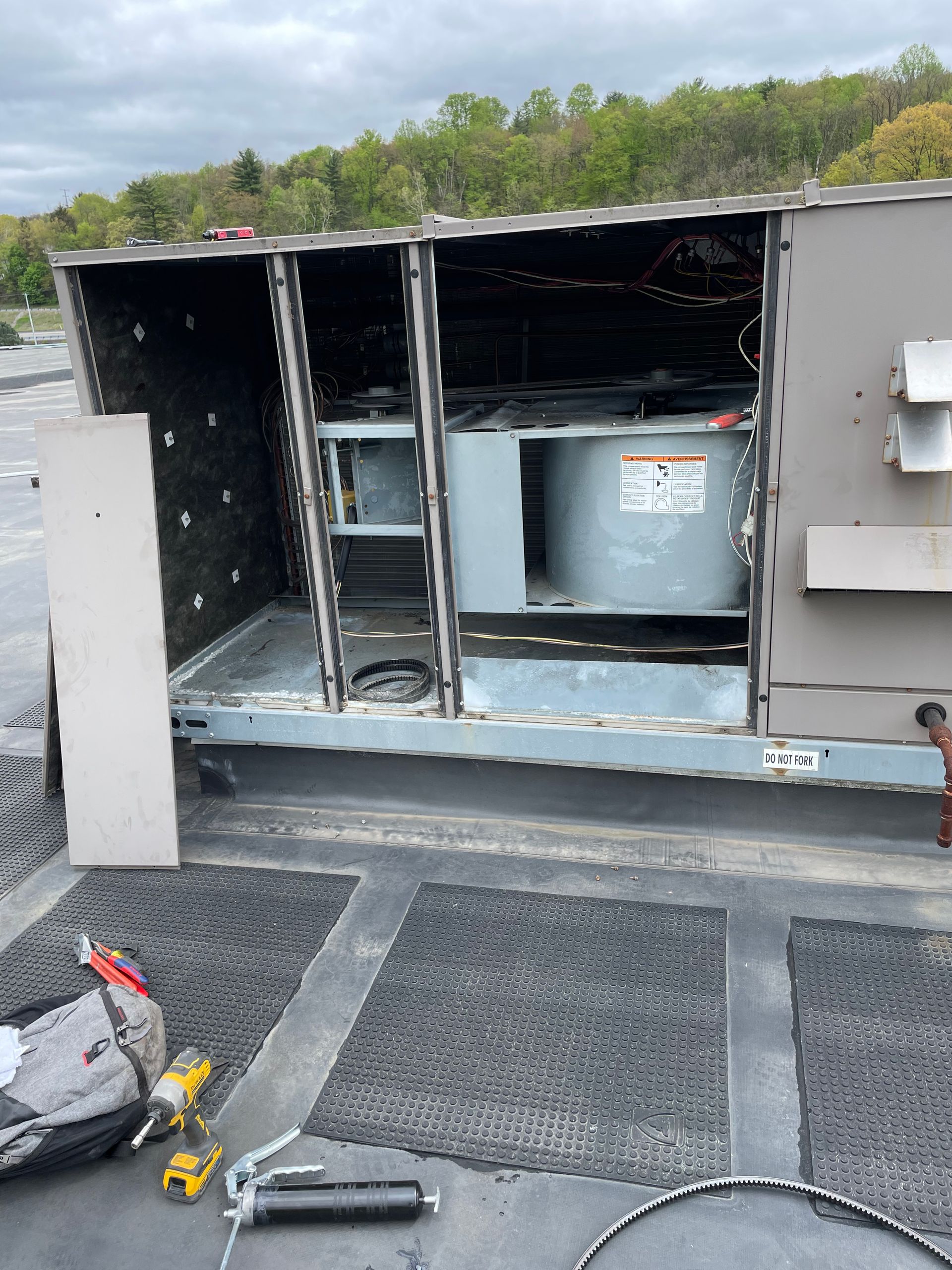 HVAC unit on a rooftop with access panel open, revealing internal components and tools. Gray, metal, outdoors.