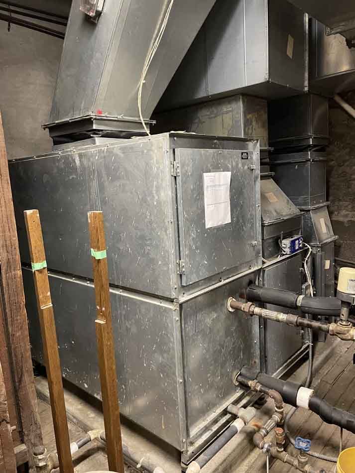 A large, industrial metal HVAC unit with ductwork in a dimly lit room.