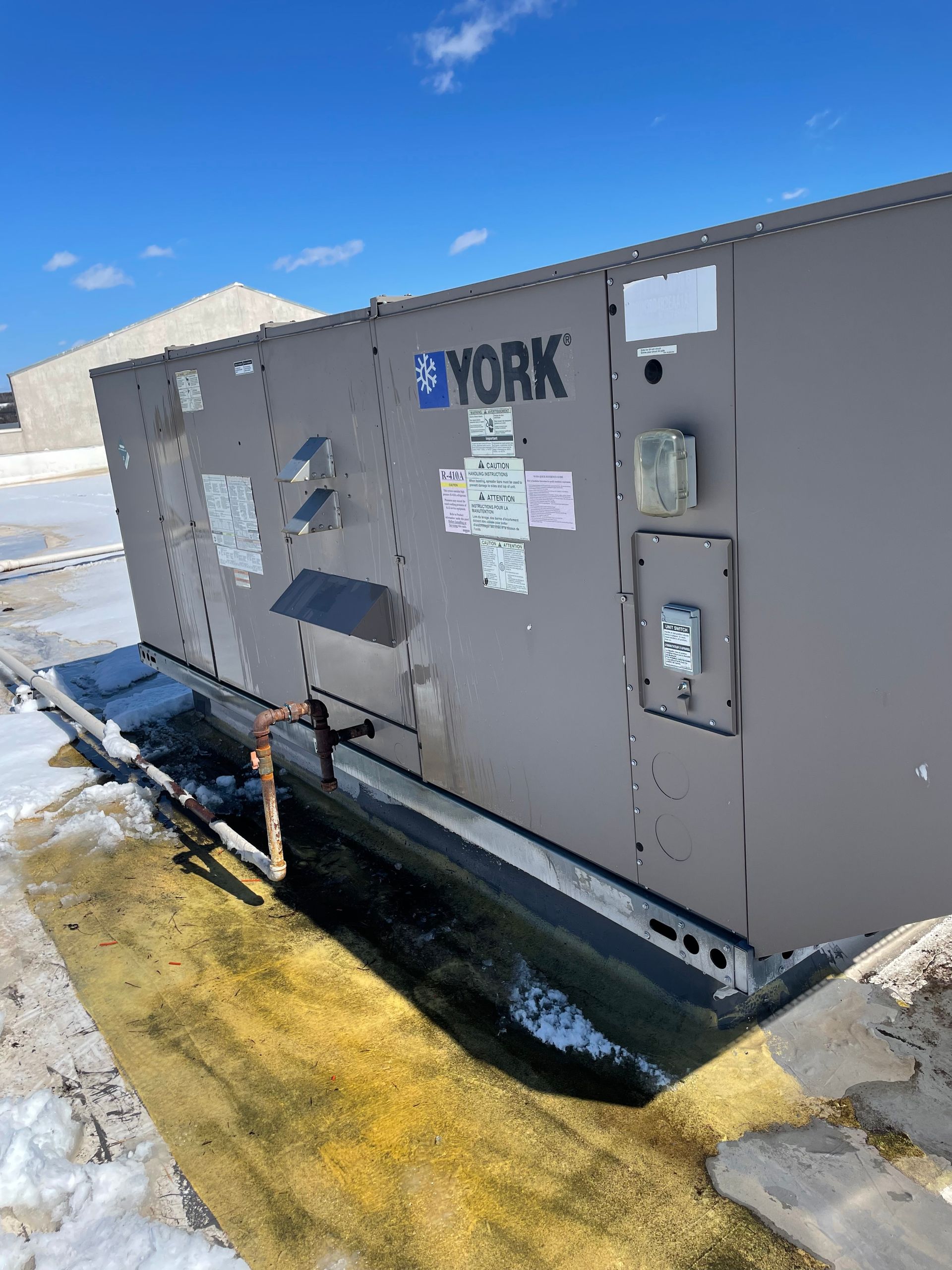 A large, gray York HVAC unit on a rooftop with patches of snow.