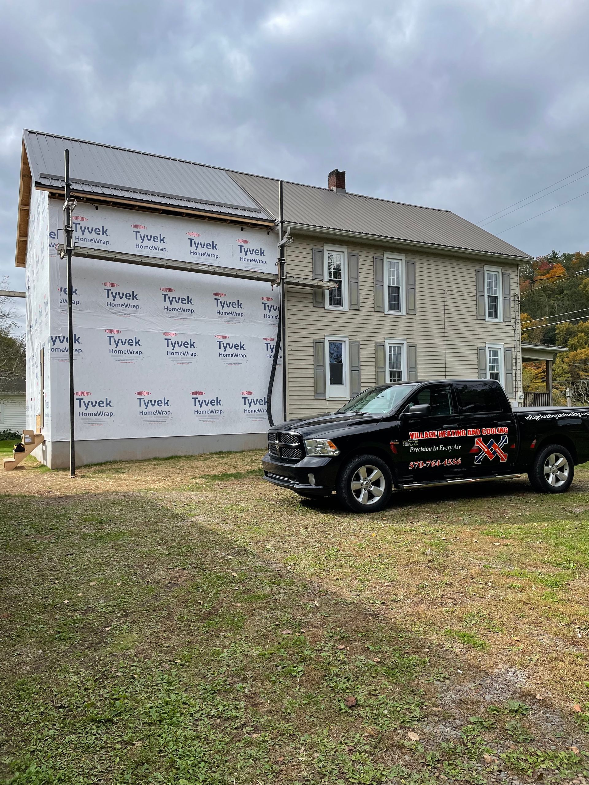 A black truck parked in front of a two-story house under renovation, with scaffolding.