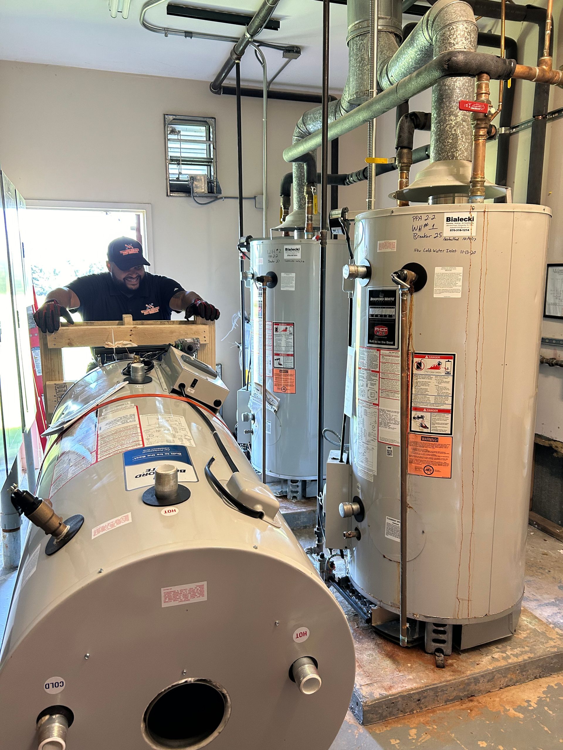Plumber working on water heaters in a utility room, with old and new tanks.
