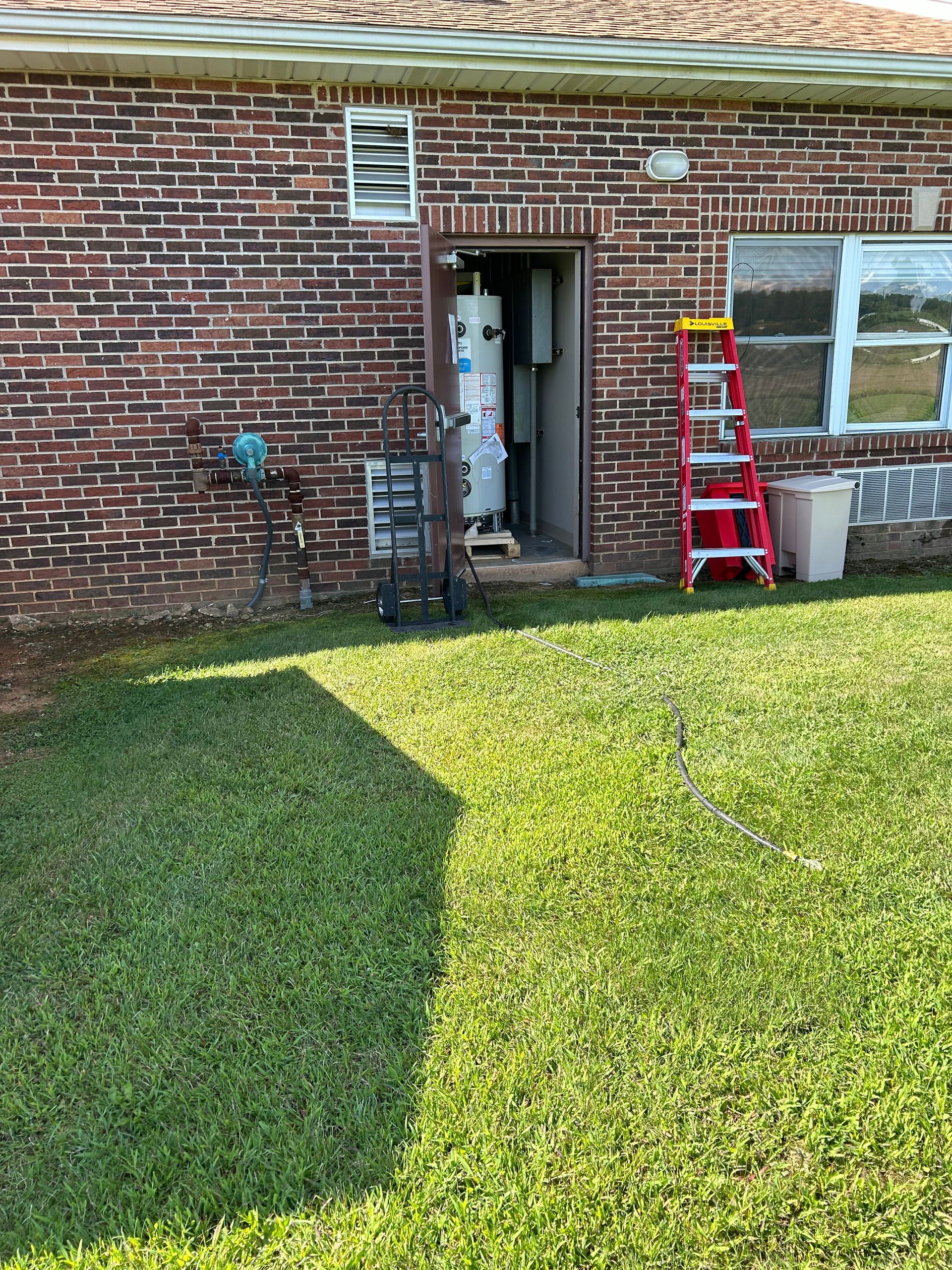 Red brick building with open doorway, ladder, and water heater on grass.