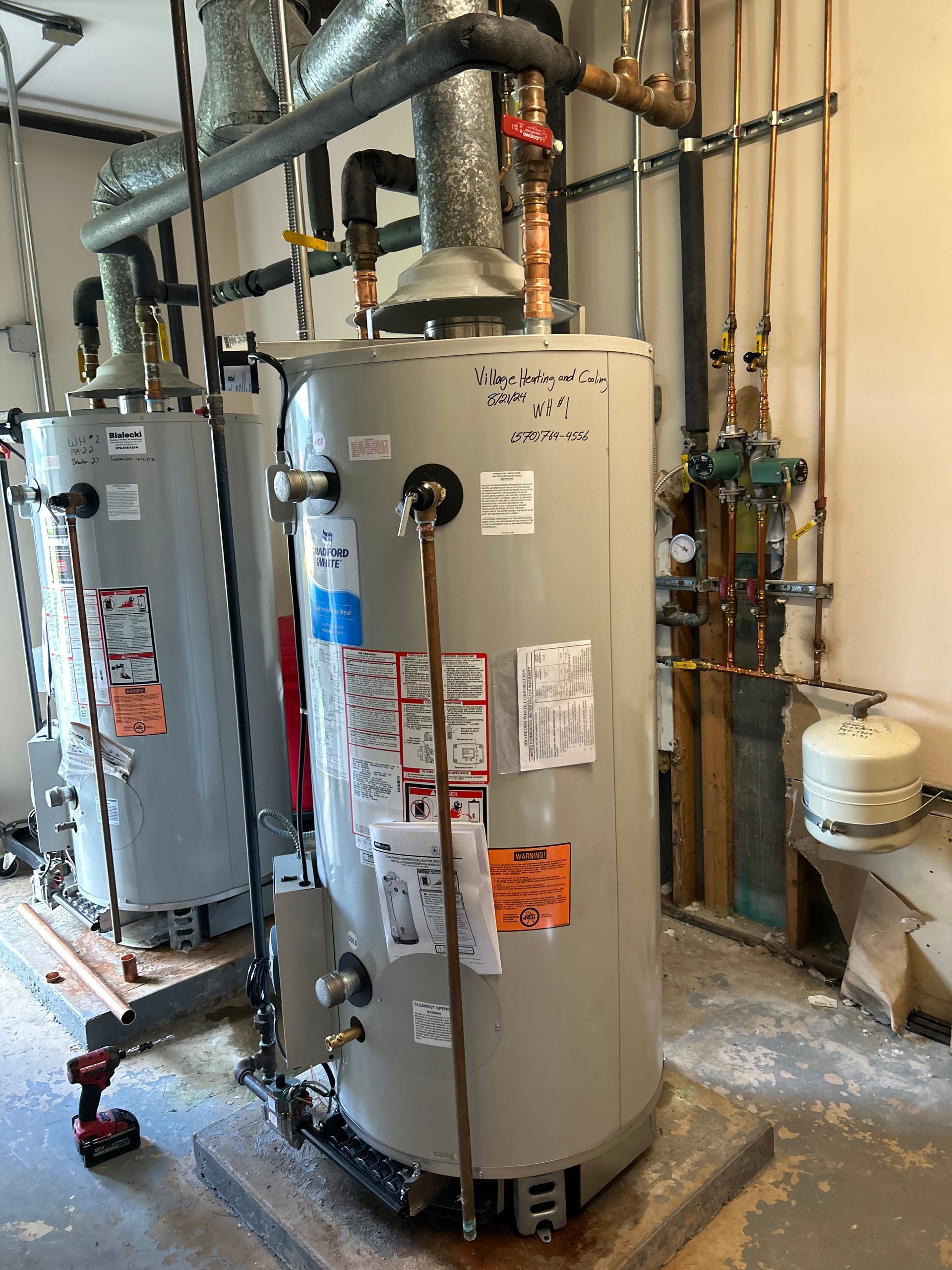 Two large, gray water heaters in a utility room with pipes and equipment.