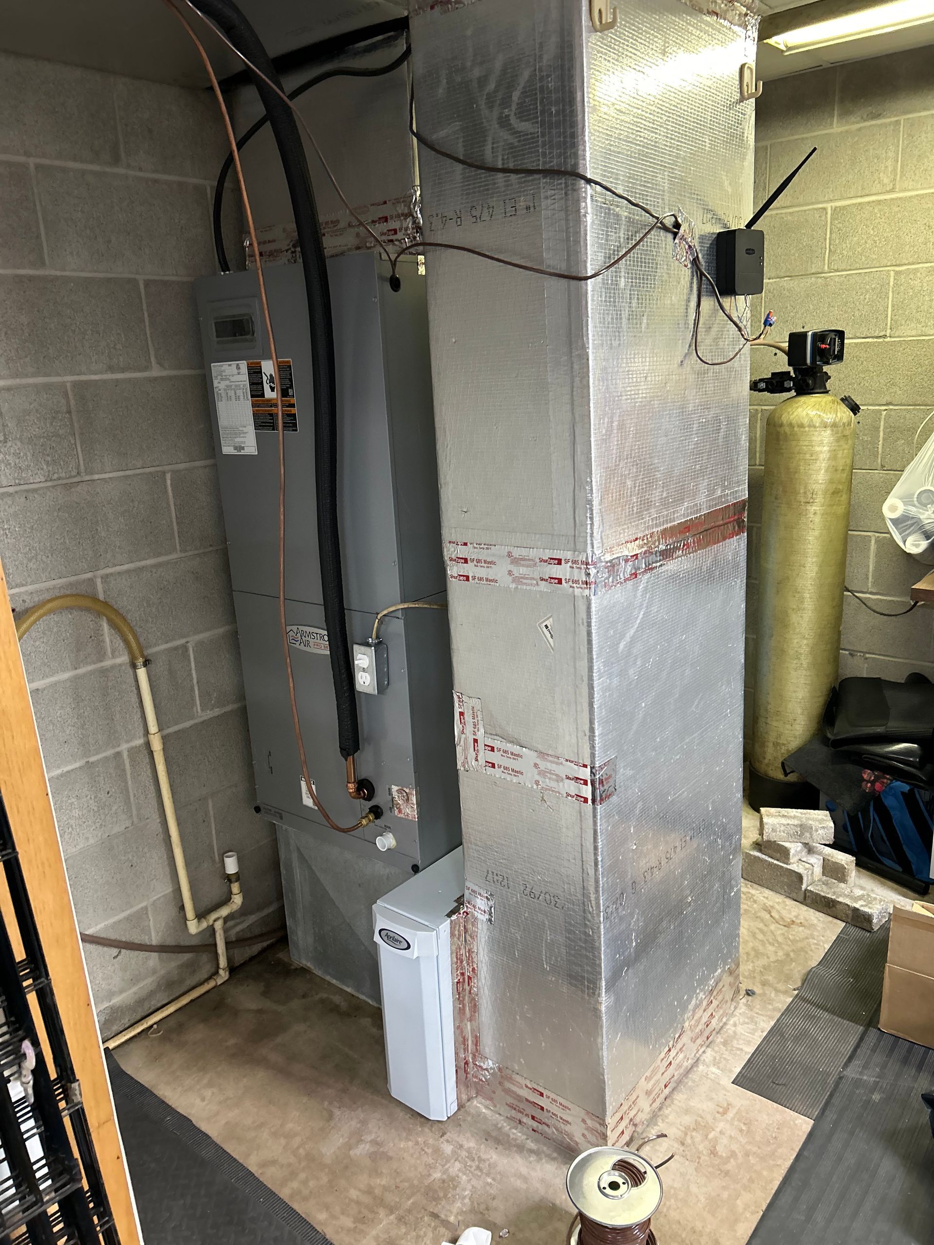 HVAC system in a utility room, with ductwork, water softener, and grey brick wall.