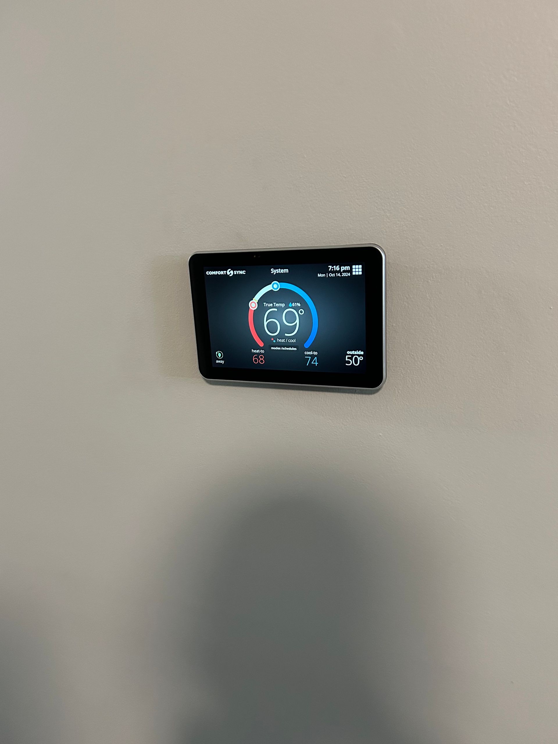 A thermostat showing a temperature of 69 degrees Fahrenheit mounted on a light gray wall.
