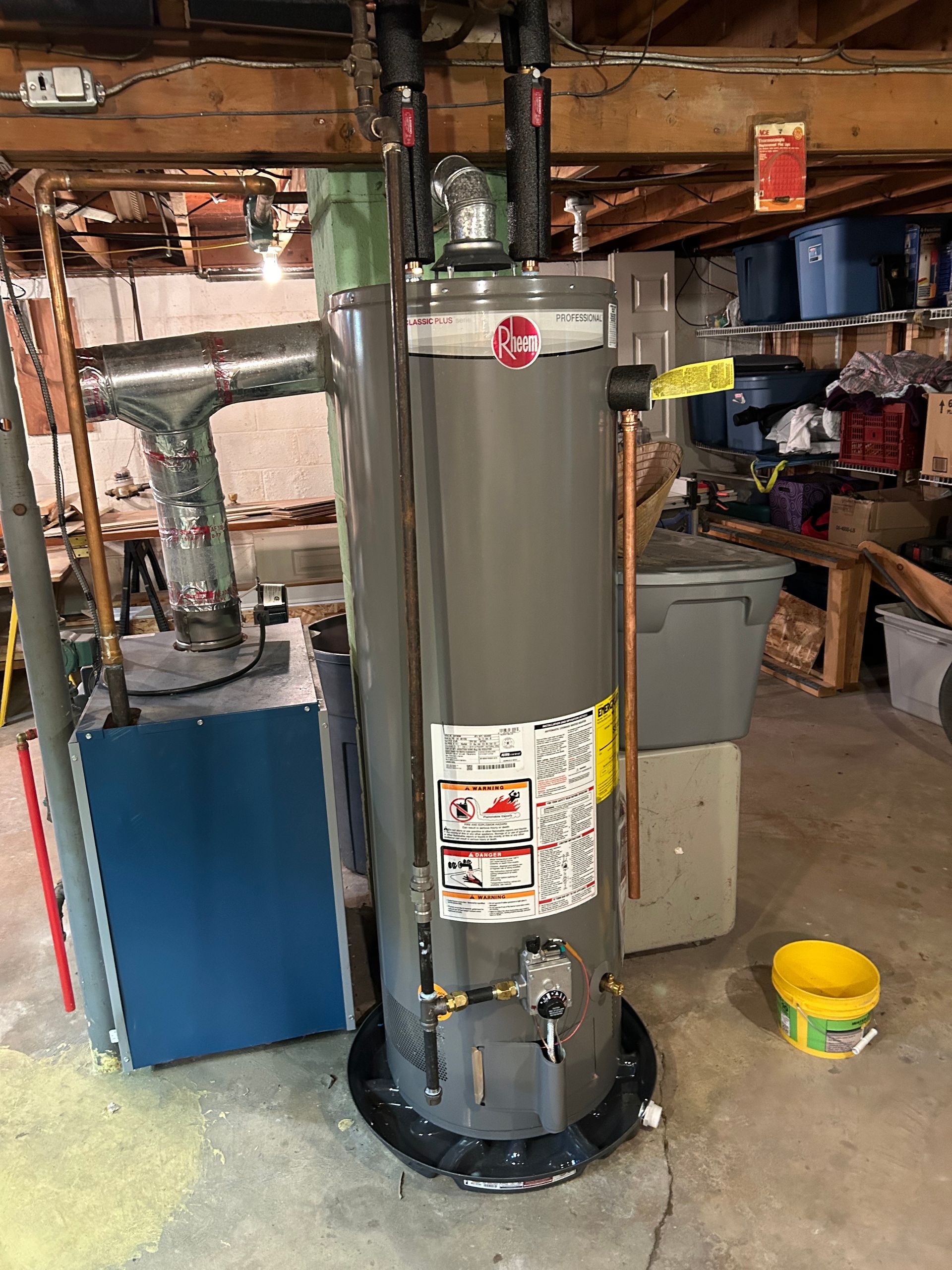 A tall, gray Rheem water heater in a cluttered basement.