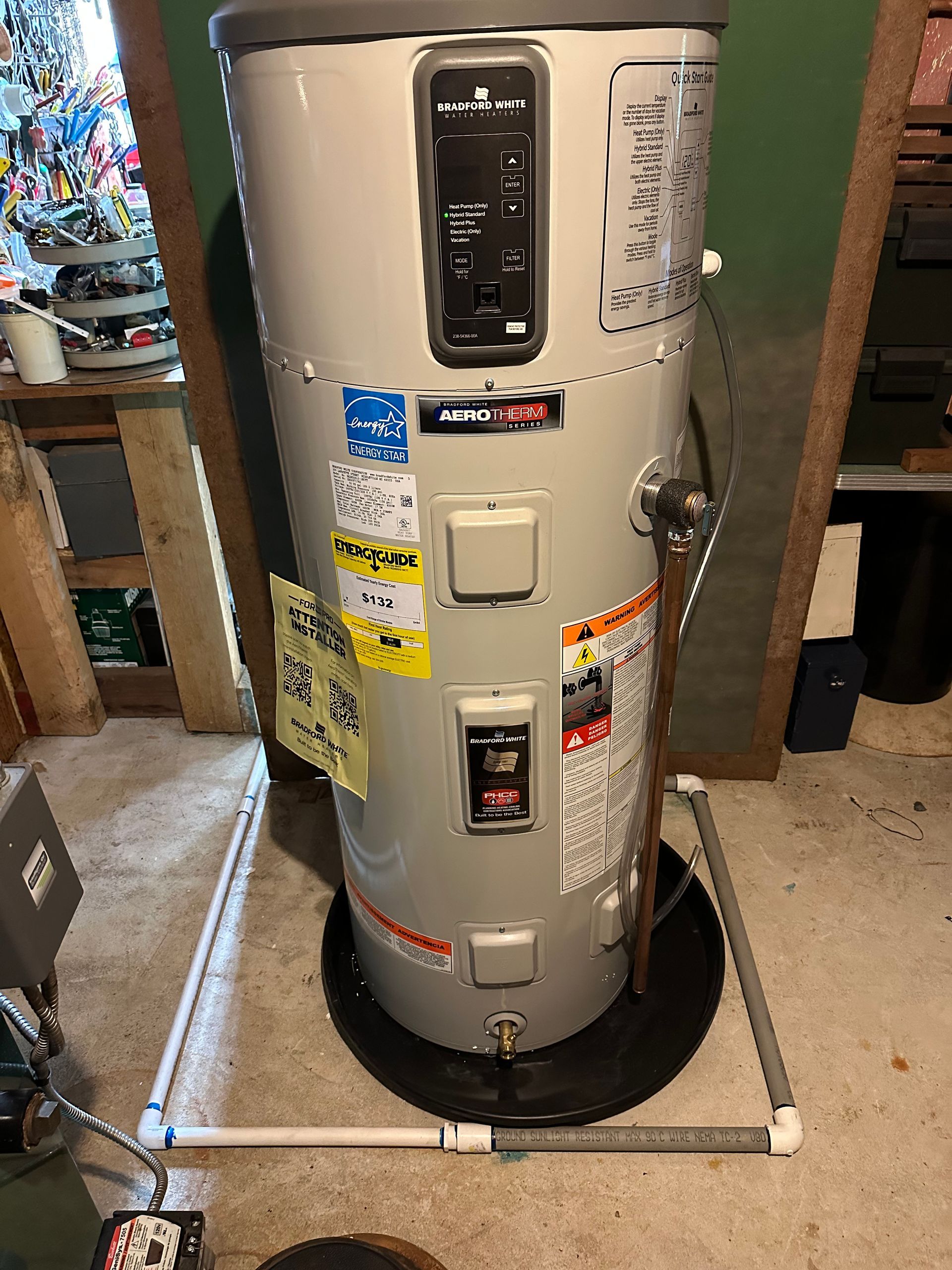 A tall, gray water heater with black control panel, in a utility room, with pipe running from the bottom.