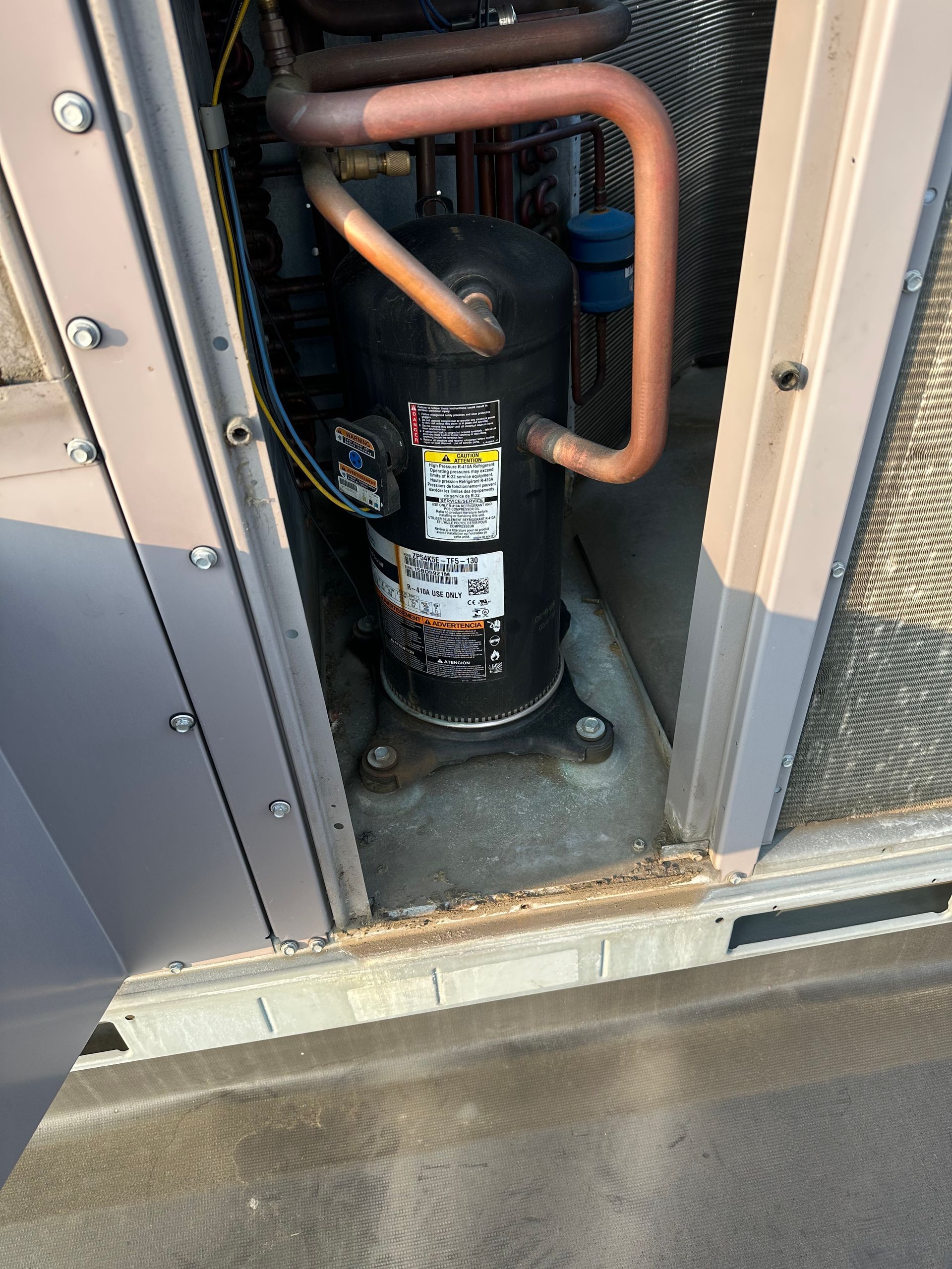Black HVAC compressor inside a gray metal unit, with copper tubing.