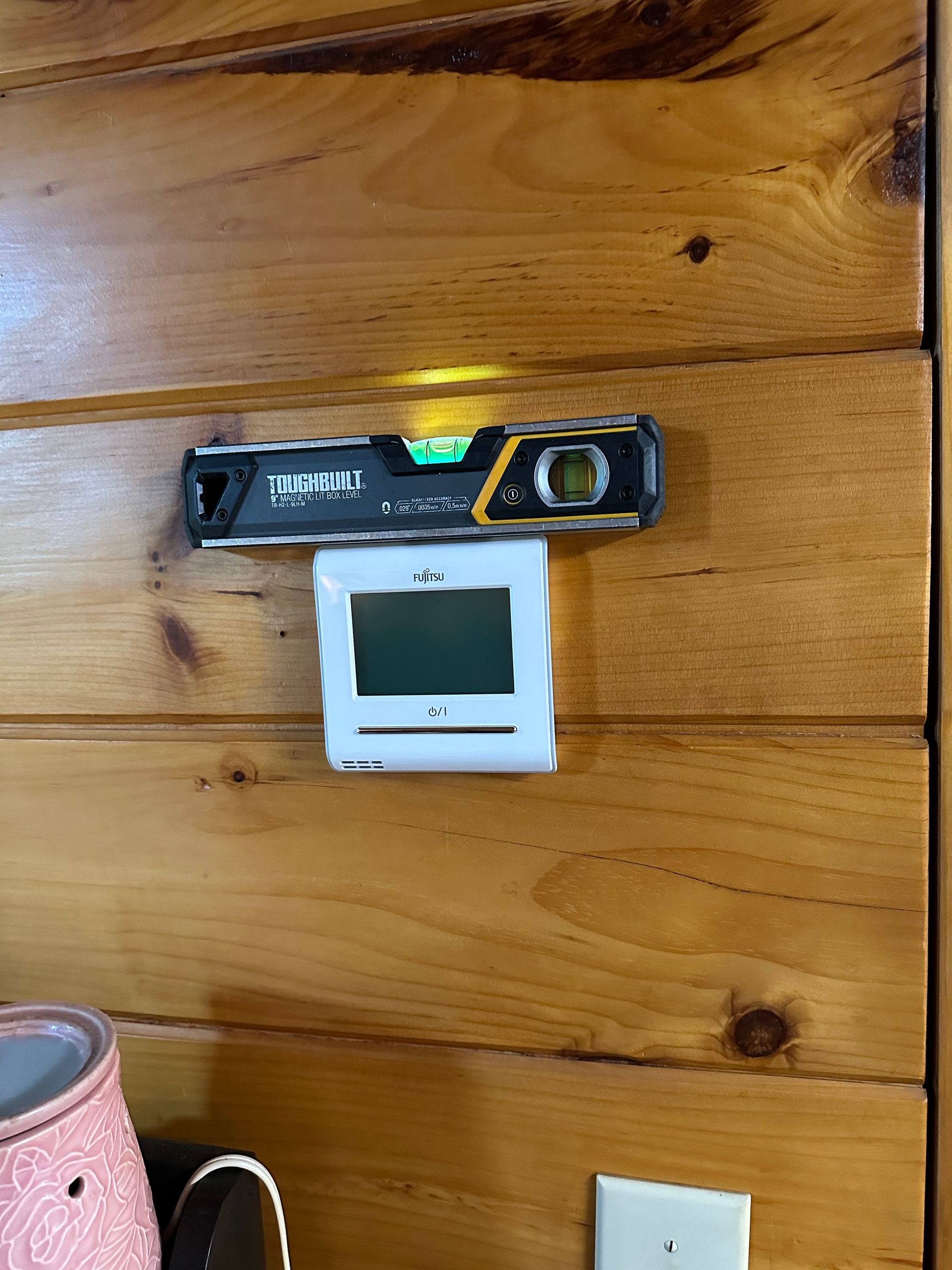 Level and thermostat mounted on a wooden wall, with a light switch visible below.