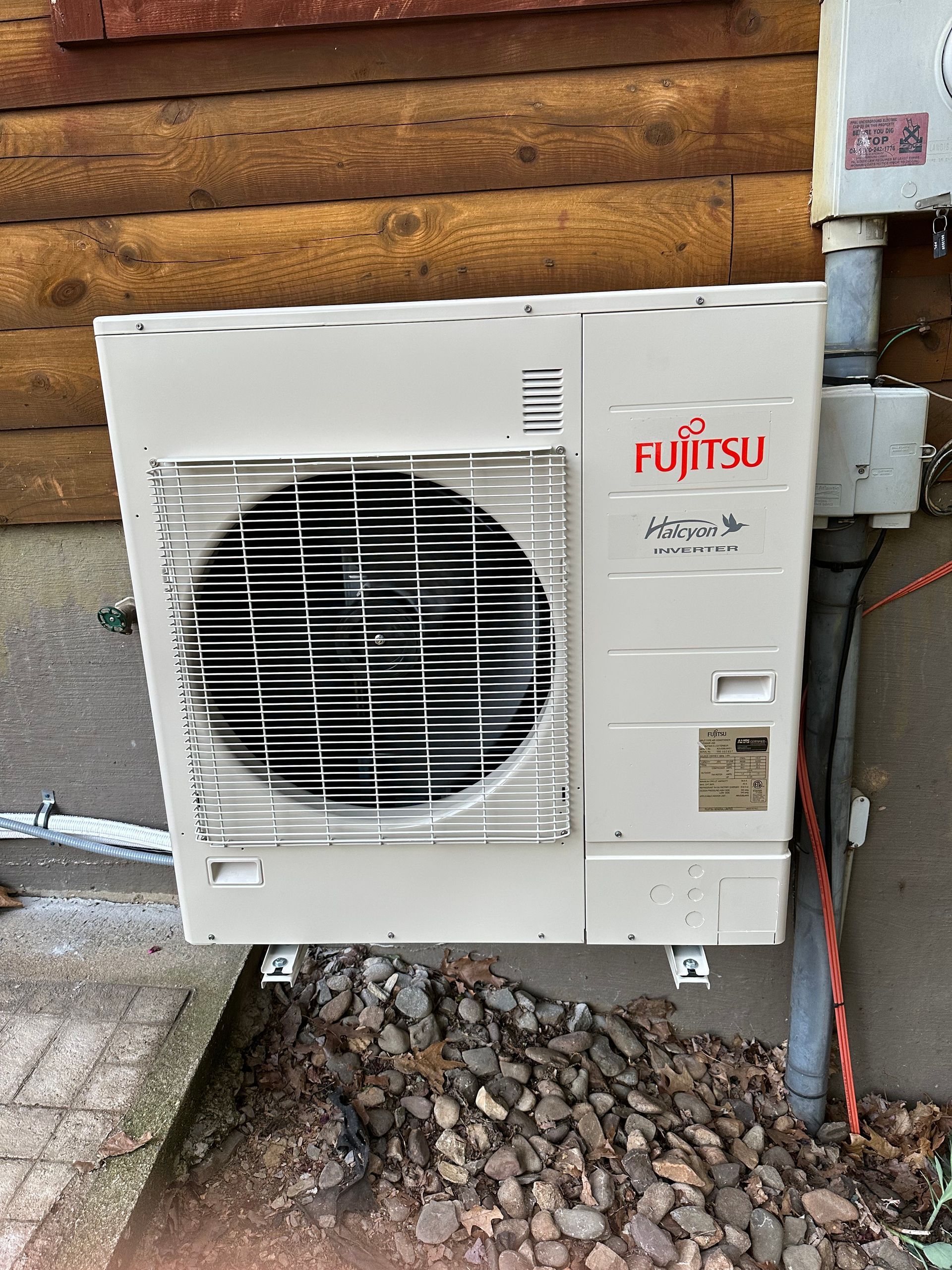 Fujitsu outdoor AC unit mounted on a wooden wall, with rocks below.