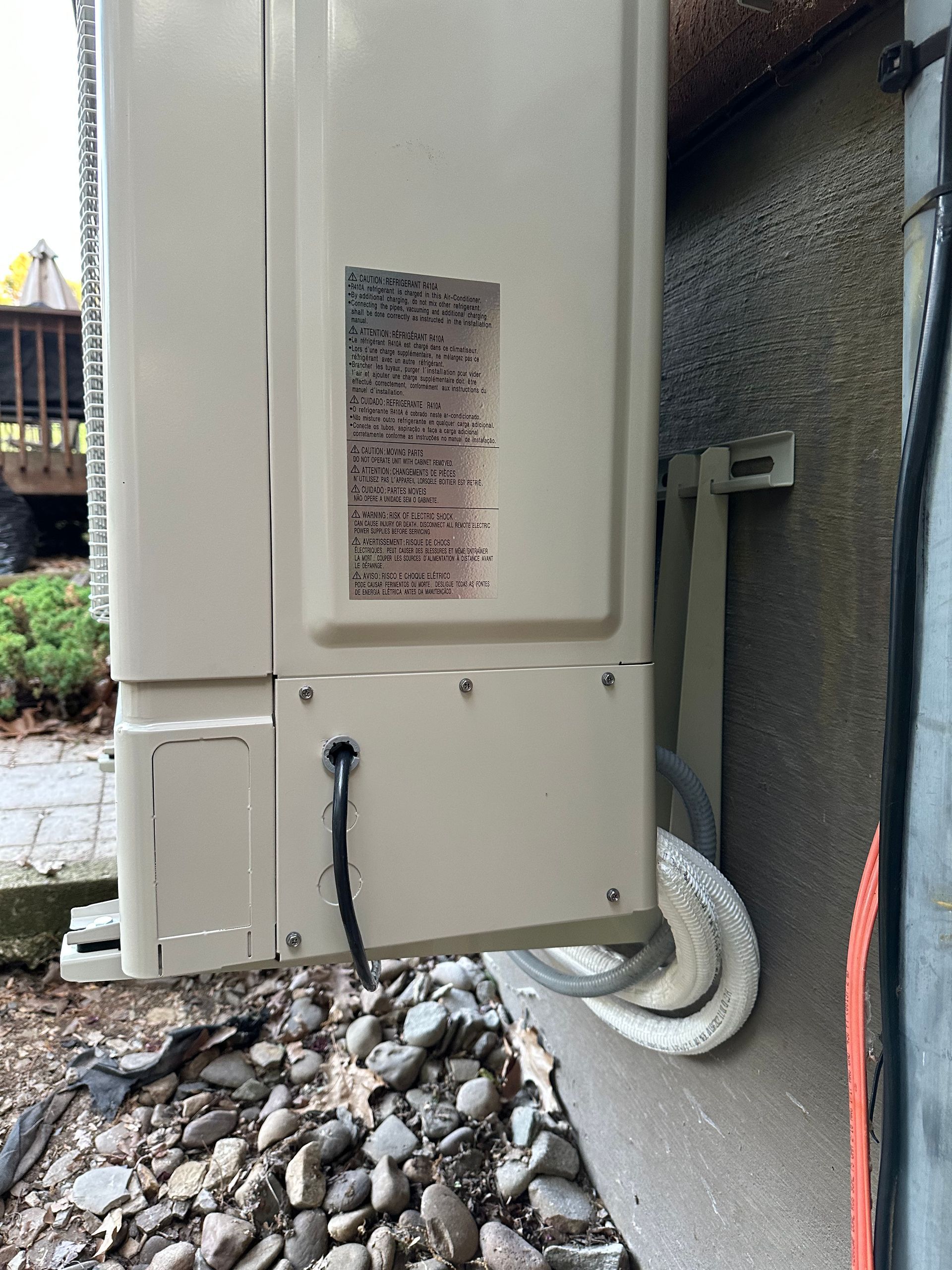 Beige air conditioning unit mounted on a textured wall, with connecting pipes.