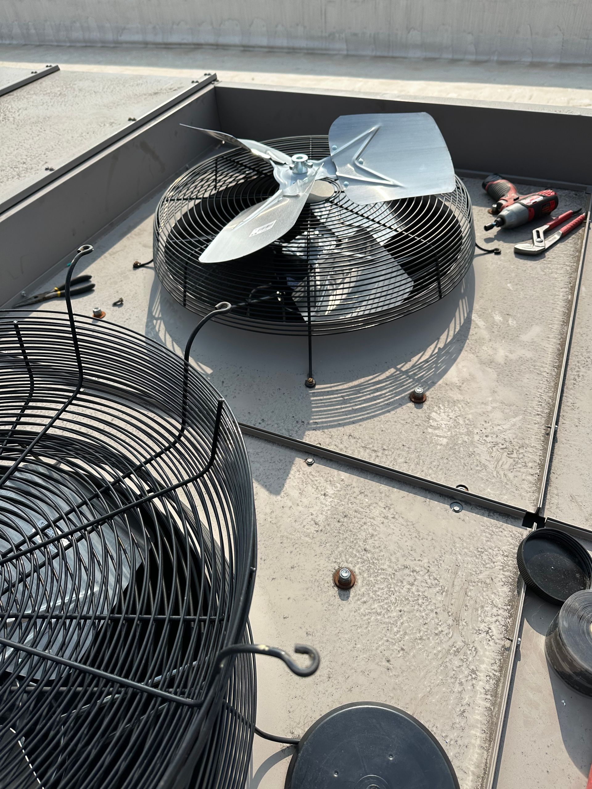 Two air conditioning units on a rooftop. One unit has fan blades exposed, tools nearby.