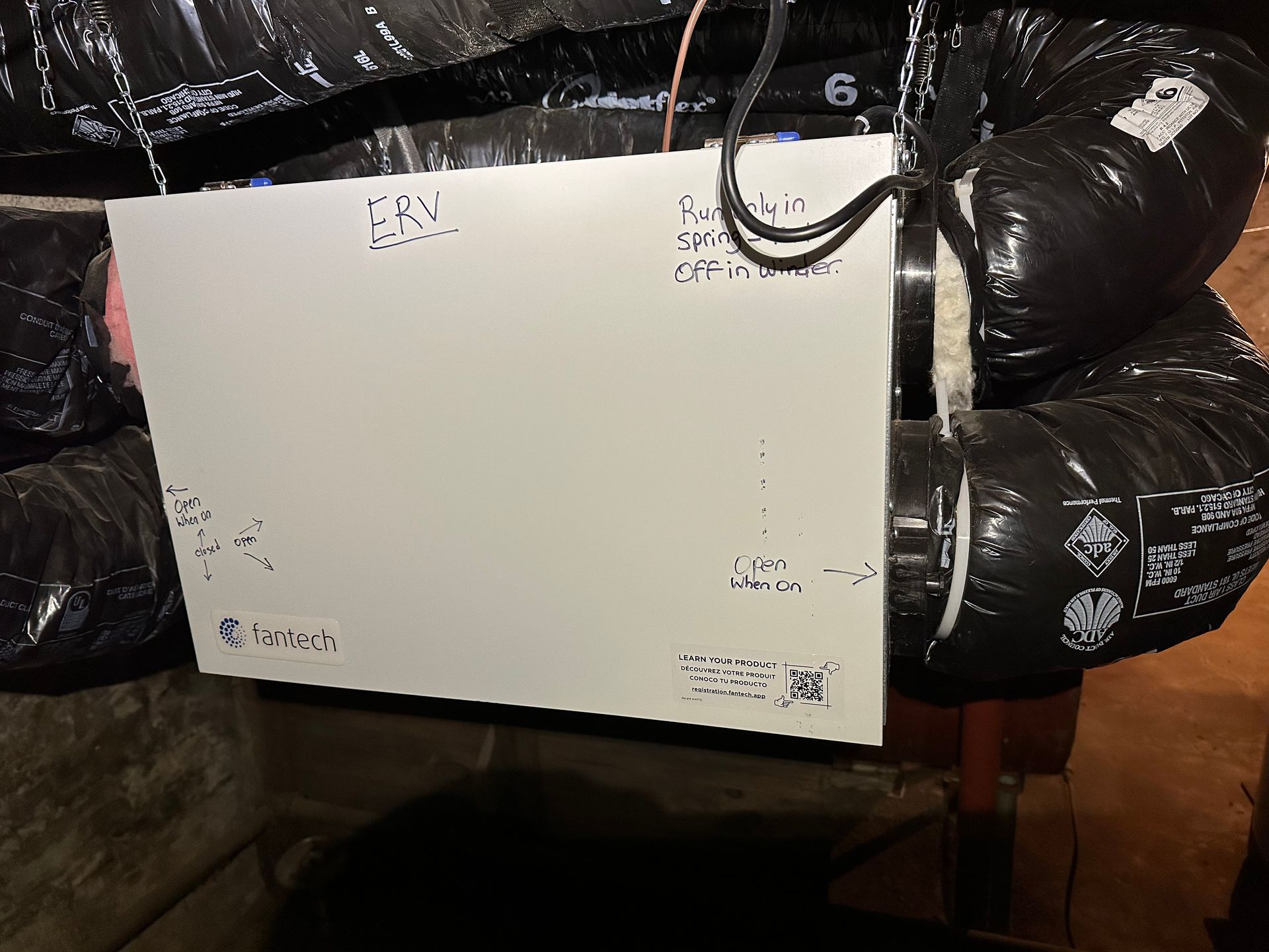 White air filter box attached to black insulated ductwork in a crawl space.