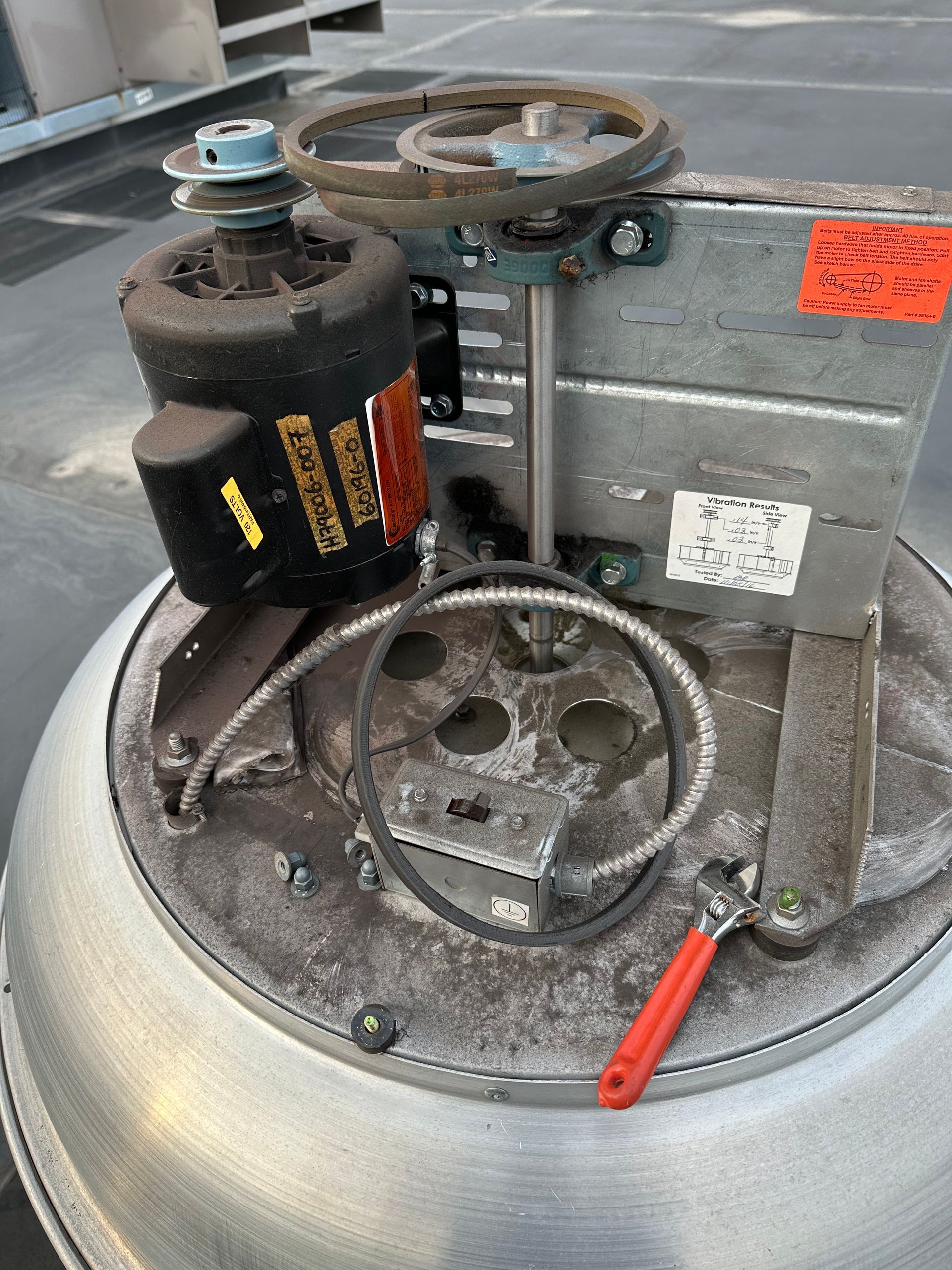 Metal mechanical device with motor, pulleys, and a belt. Gray, black, and red components sit on a rounded surface.