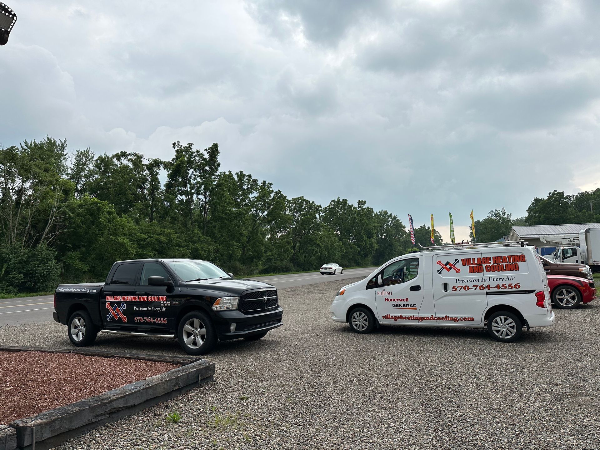 Black truck and white van with business logos parked in a gravel lot on a cloudy day.