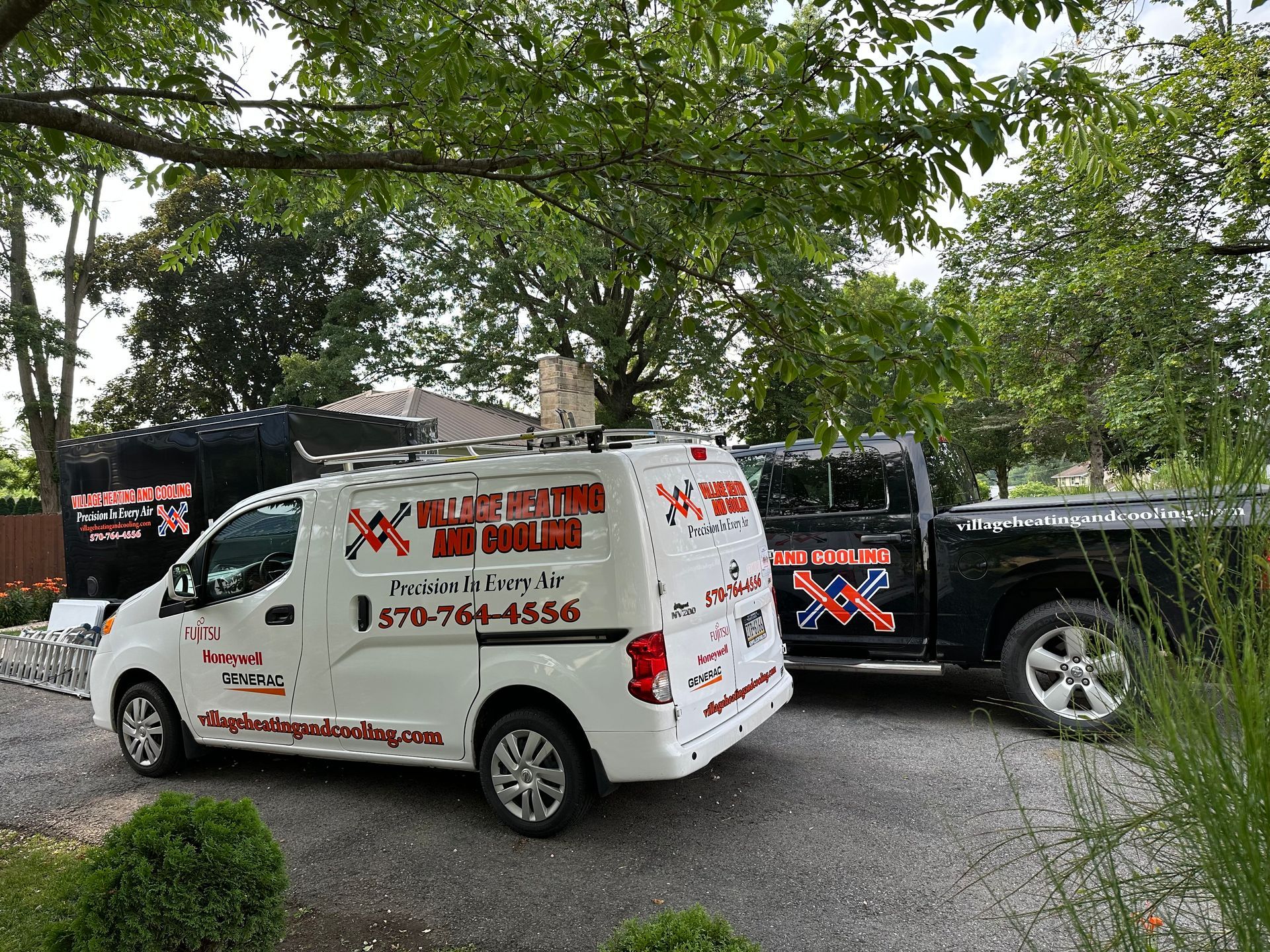 White van and black truck with company logos, parked next to each other. The van has a roof rack.