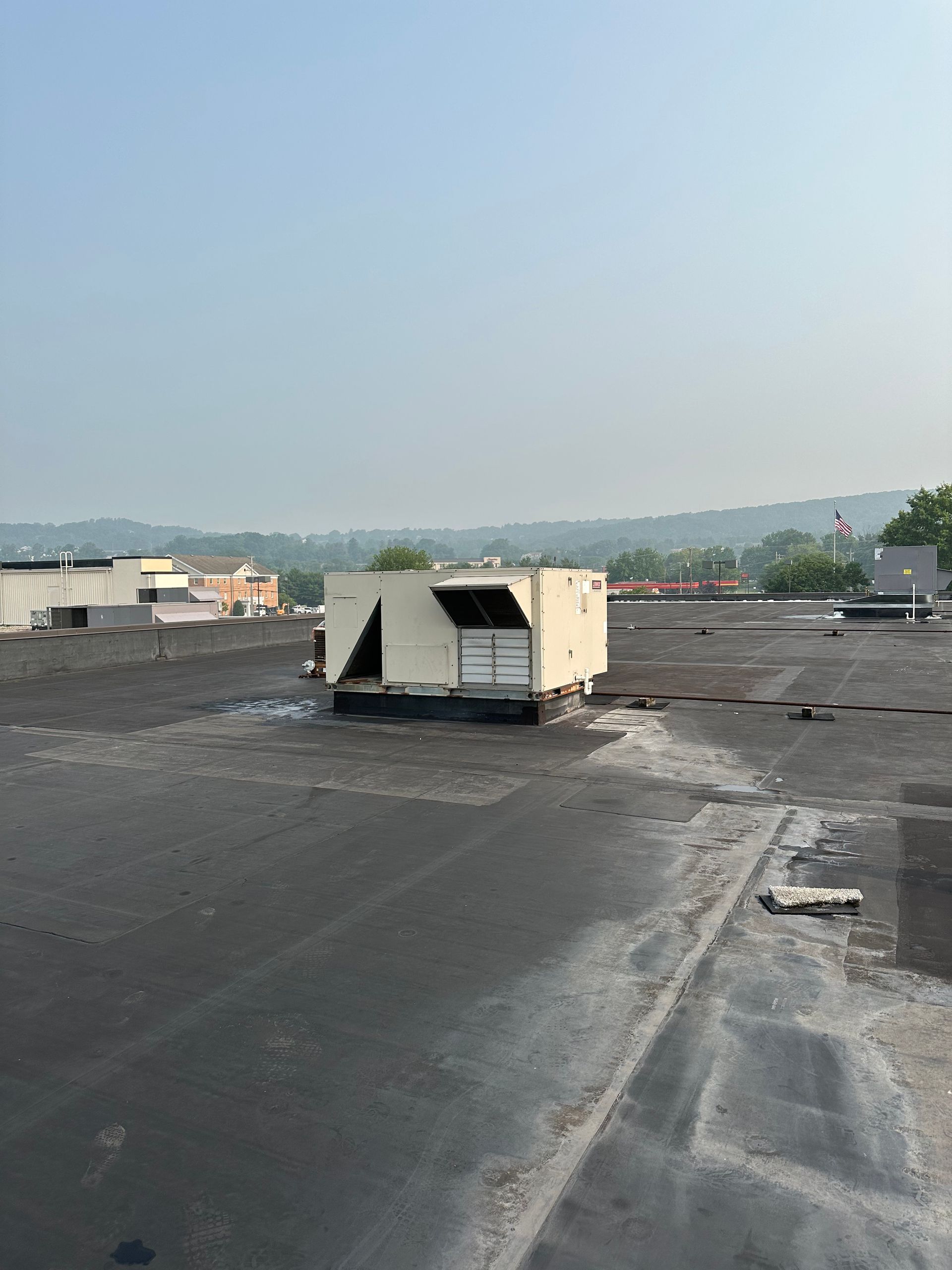 Rooftop with an air conditioning unit in the center. Hills are visible in the background under a hazy sky.