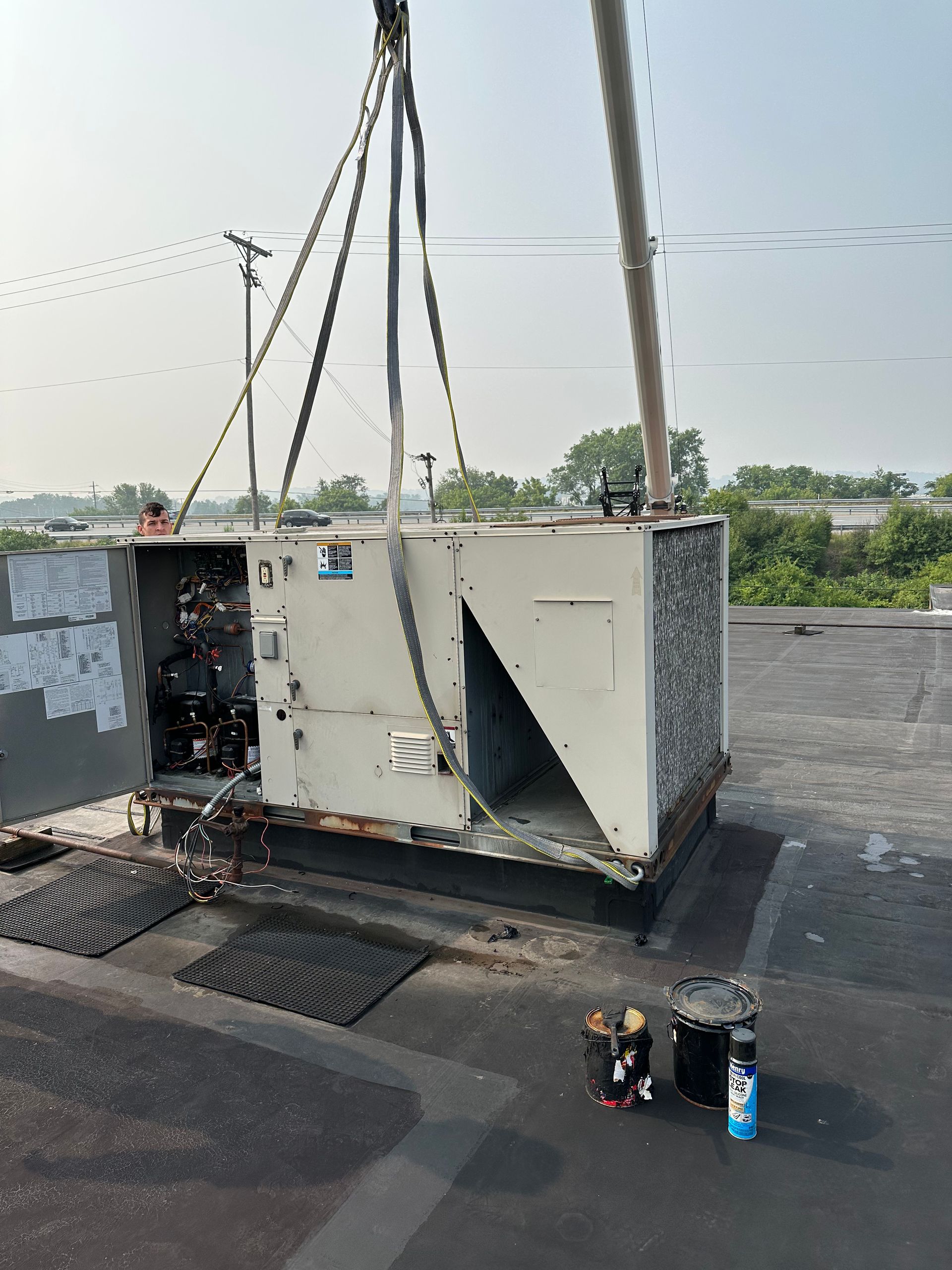 HVAC unit being lifted by crane on a roof; tools and equipment visible.