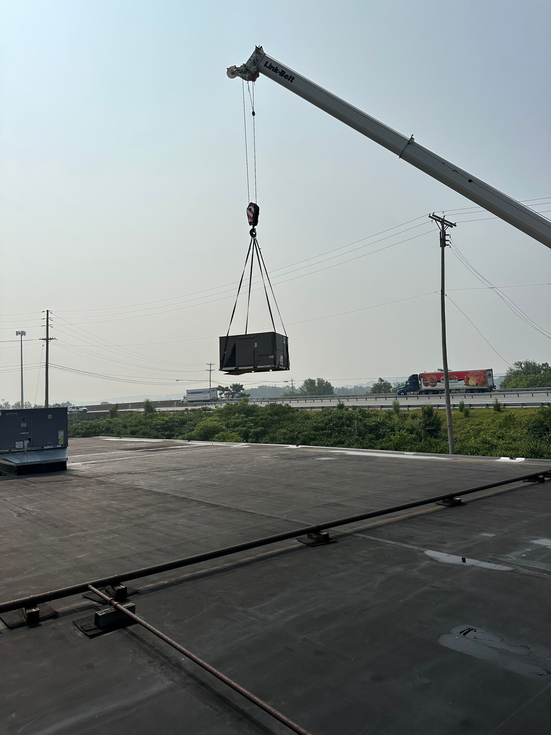 A crane lifting a dark container outdoors on a paved area with a truck nearby.