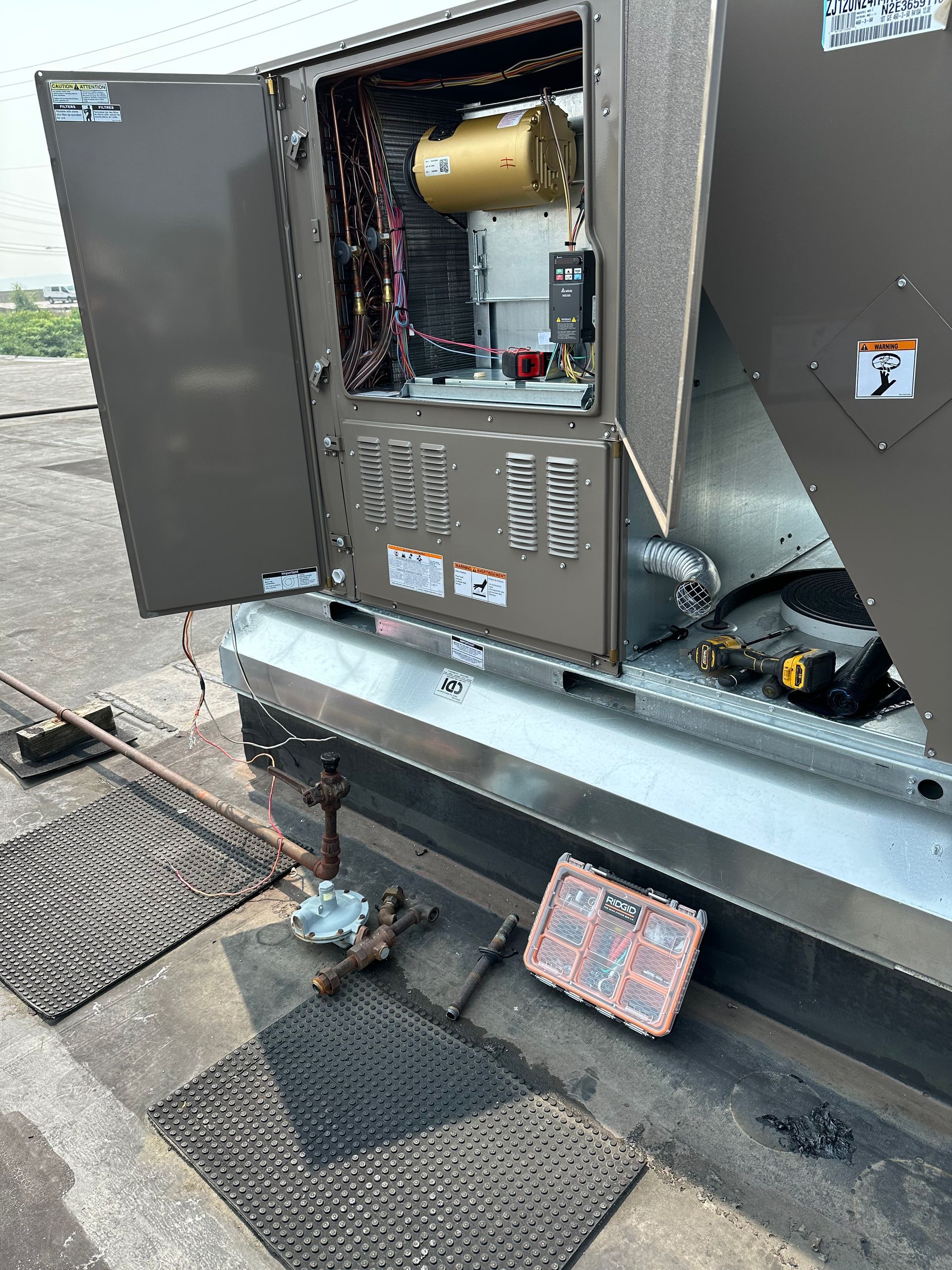 Rooftop air conditioning unit with open access panel. Tools and parts on the roof.