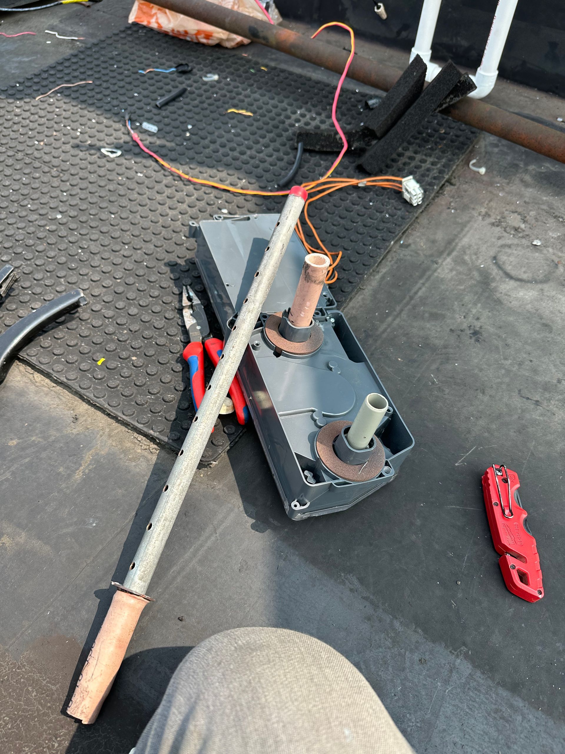 Disassembled car part with wires, pliers, and a metal rod on a dark surface. A red knife lies to the side.