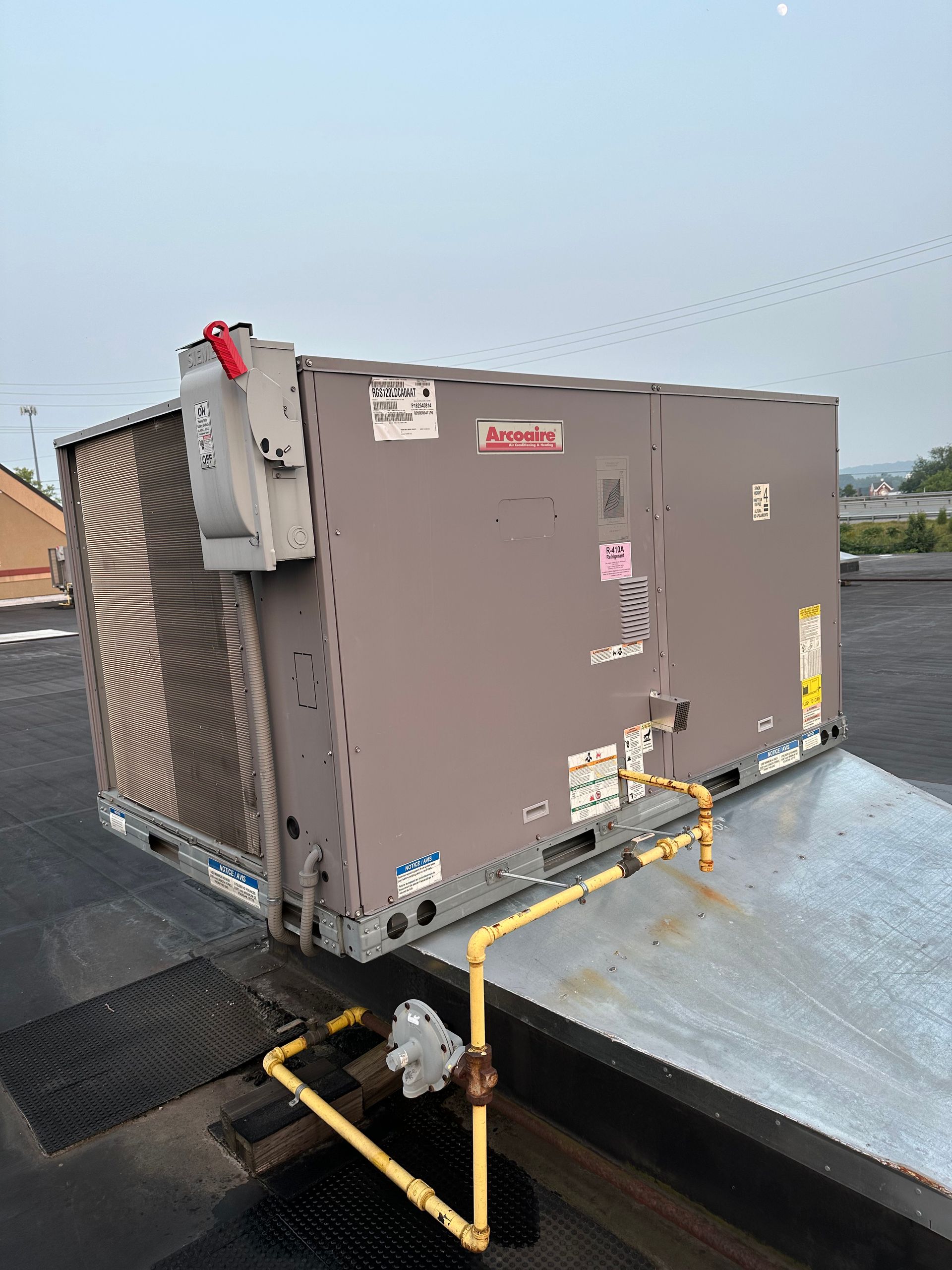 Rooftop HVAC unit with a fan, gas pipes, and control panel. Cloudy sky in background.