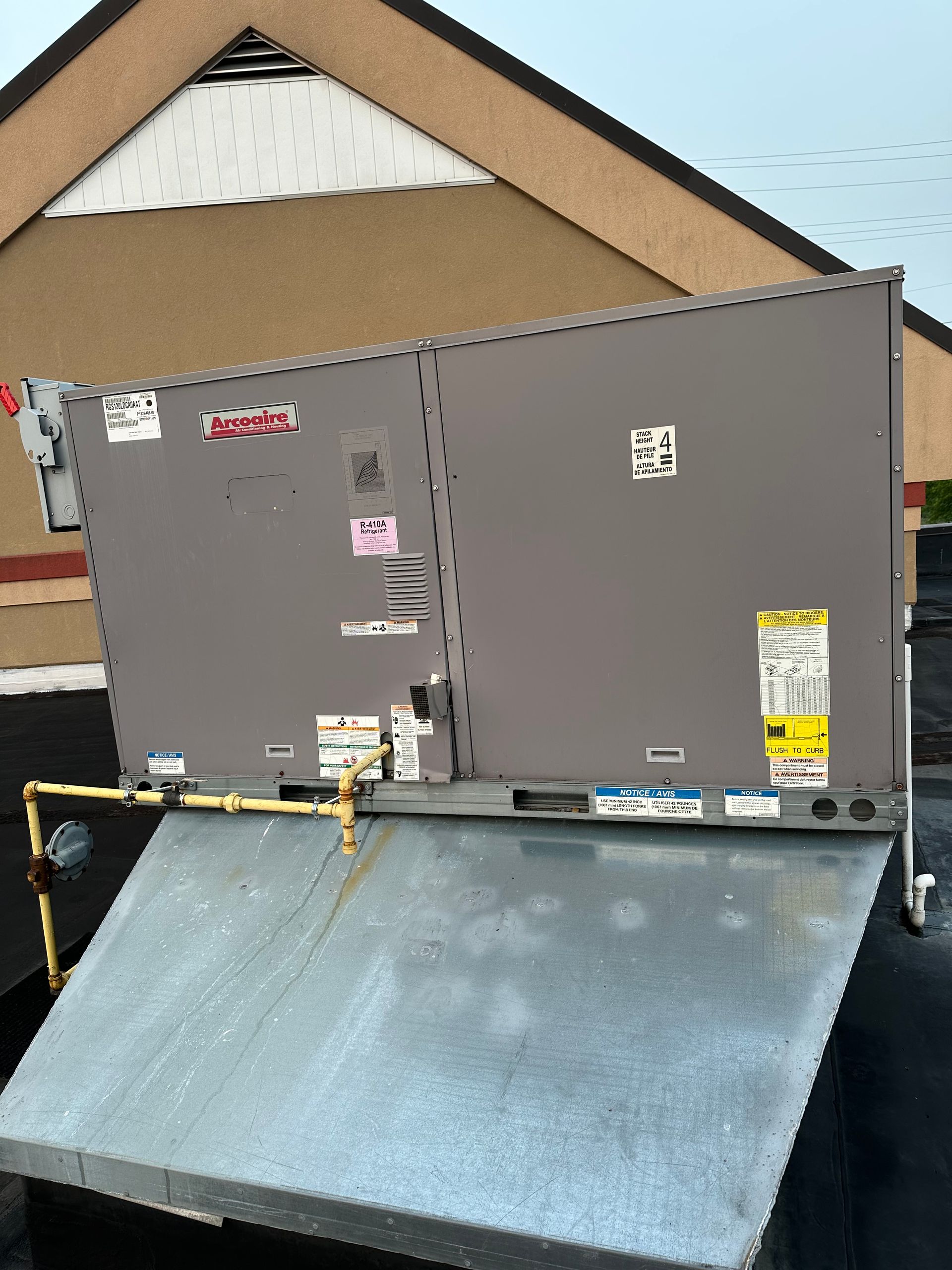 Gray rooftop HVAC unit on a metal base, against a light brown building.
