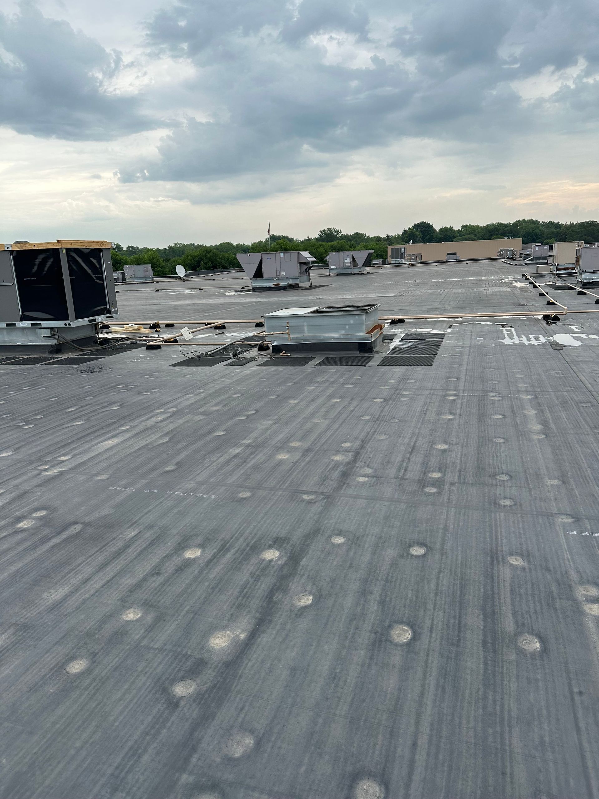 A rooftop with HVAC units against a cloudy sky. Gray and black roofing material with visible fasteners.
