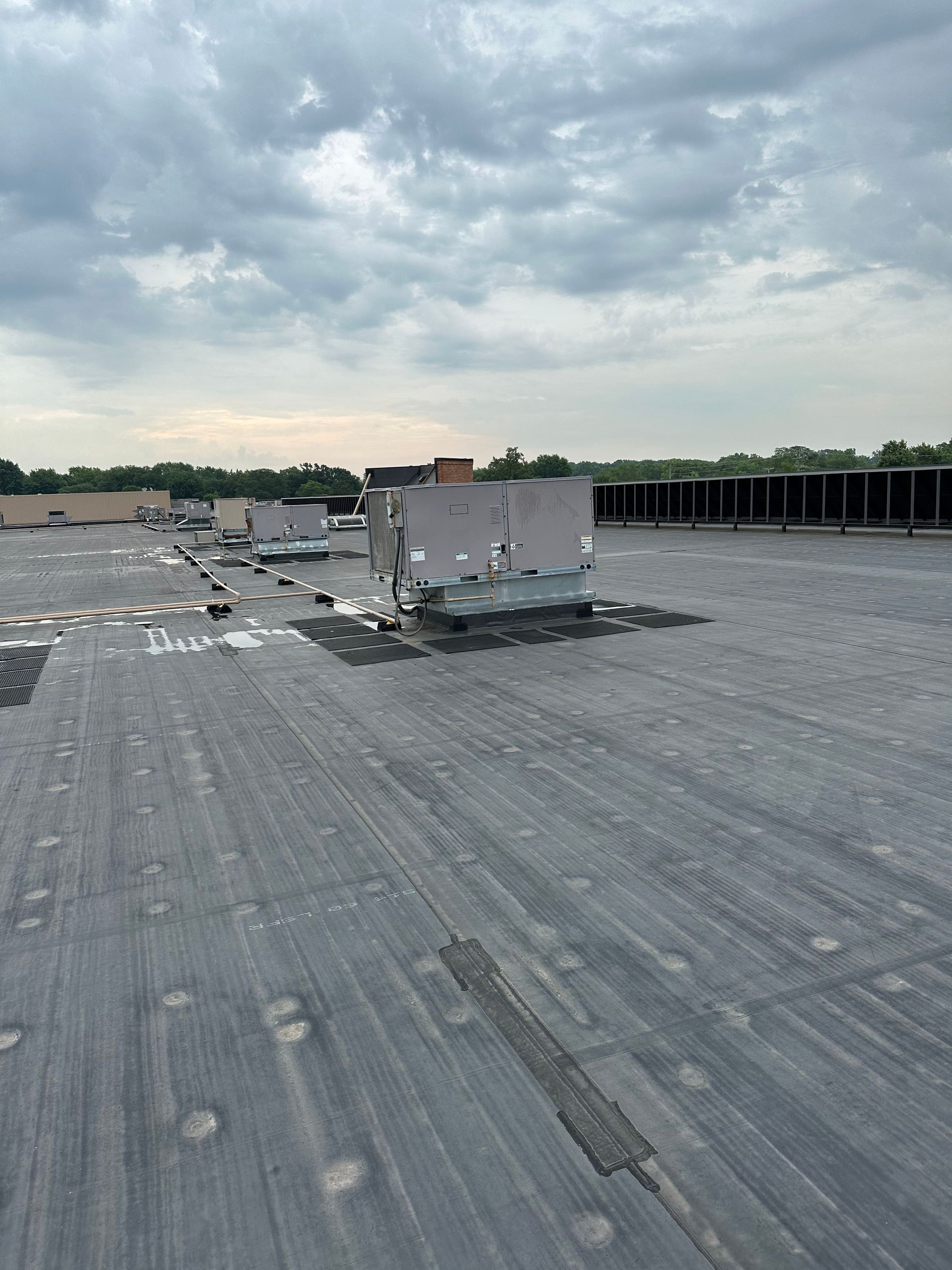 Gray rooftop with HVAC units under a cloudy sky, setting is a commercial building.
