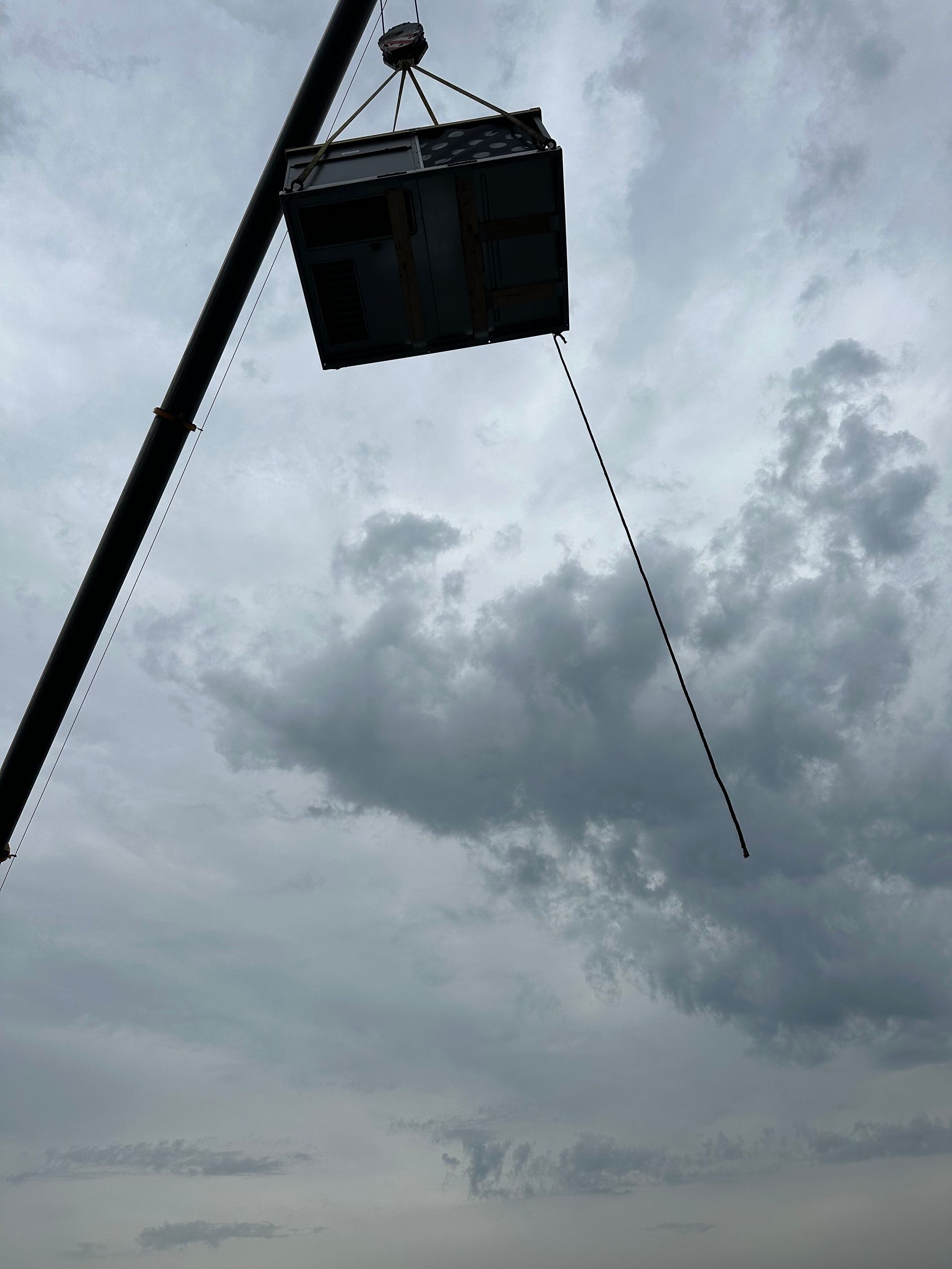 Crane lifting a metal box against a cloudy sky.