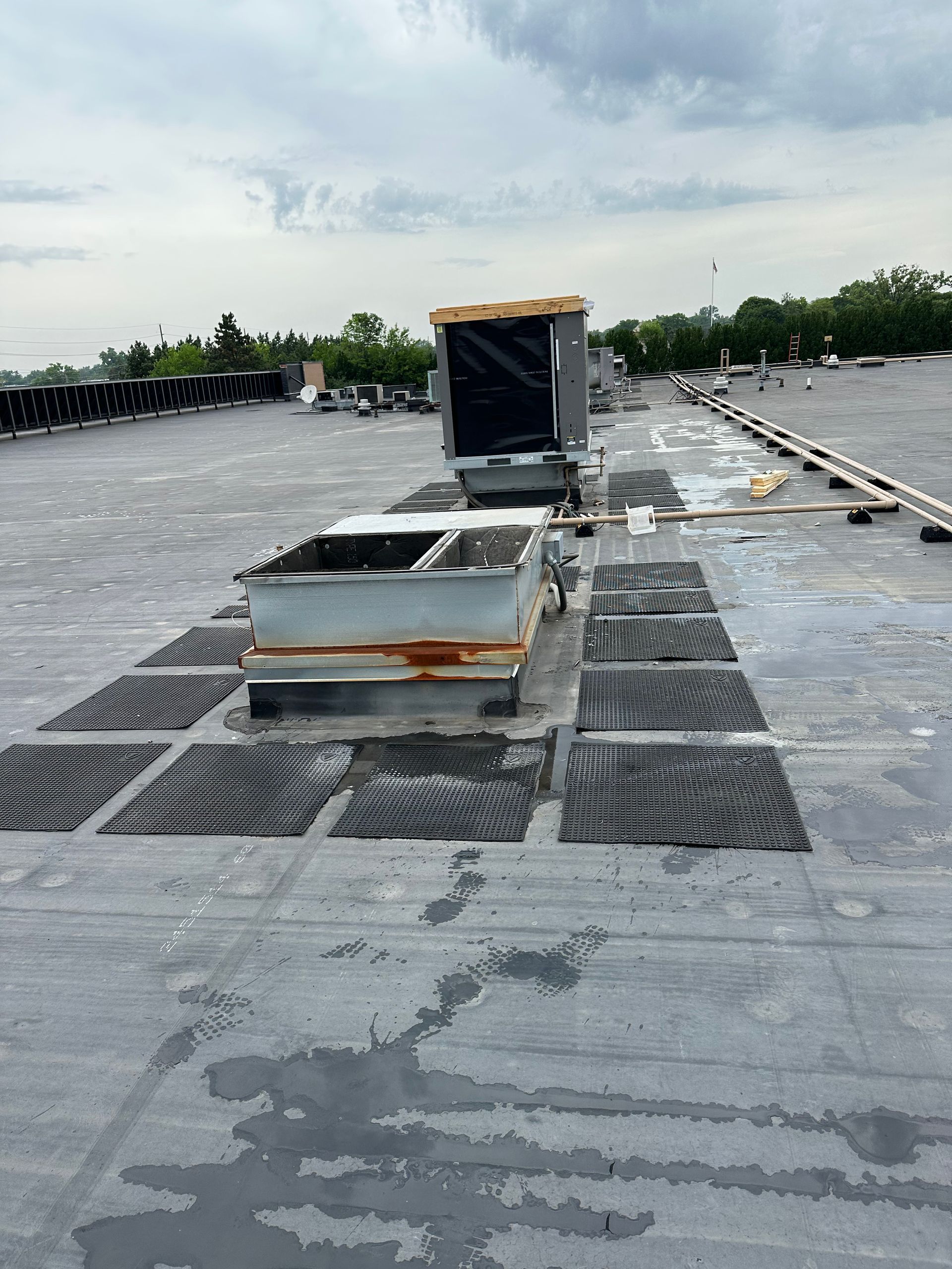 Rooftop with HVAC units, wet patches, and dark grates on a cloudy day.