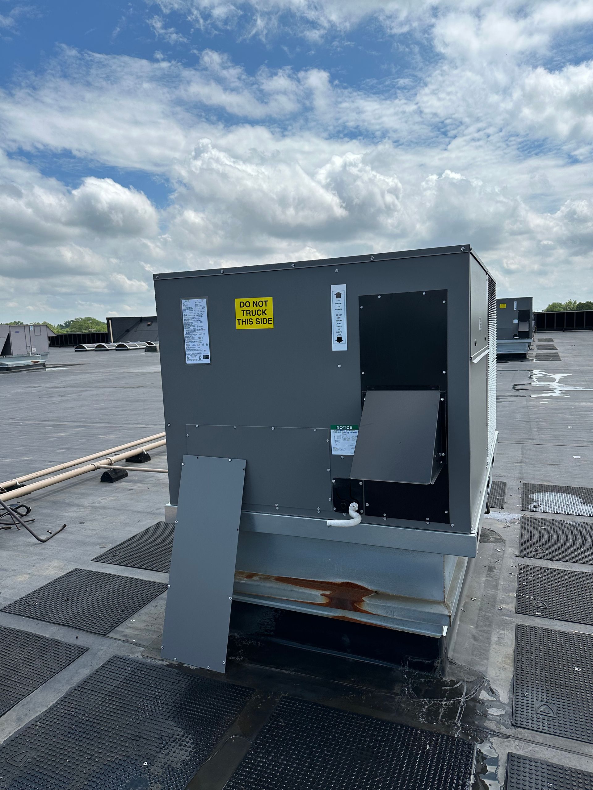 Rooftop HVAC unit; gray, rectangular on a dark rooftop with cloudy sky background.