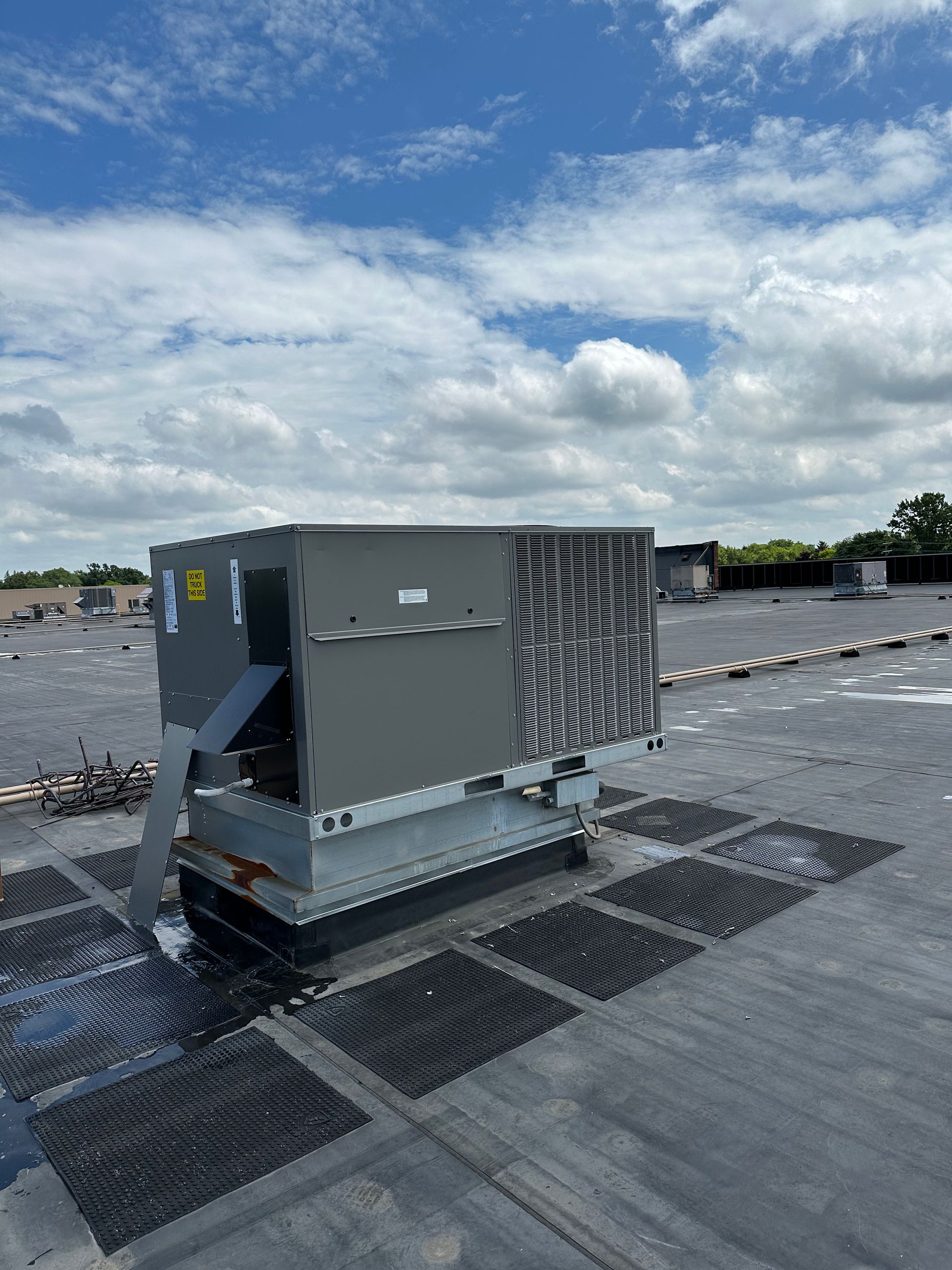 Rooftop air conditioning unit on a dark roof with a blue sky and clouds.