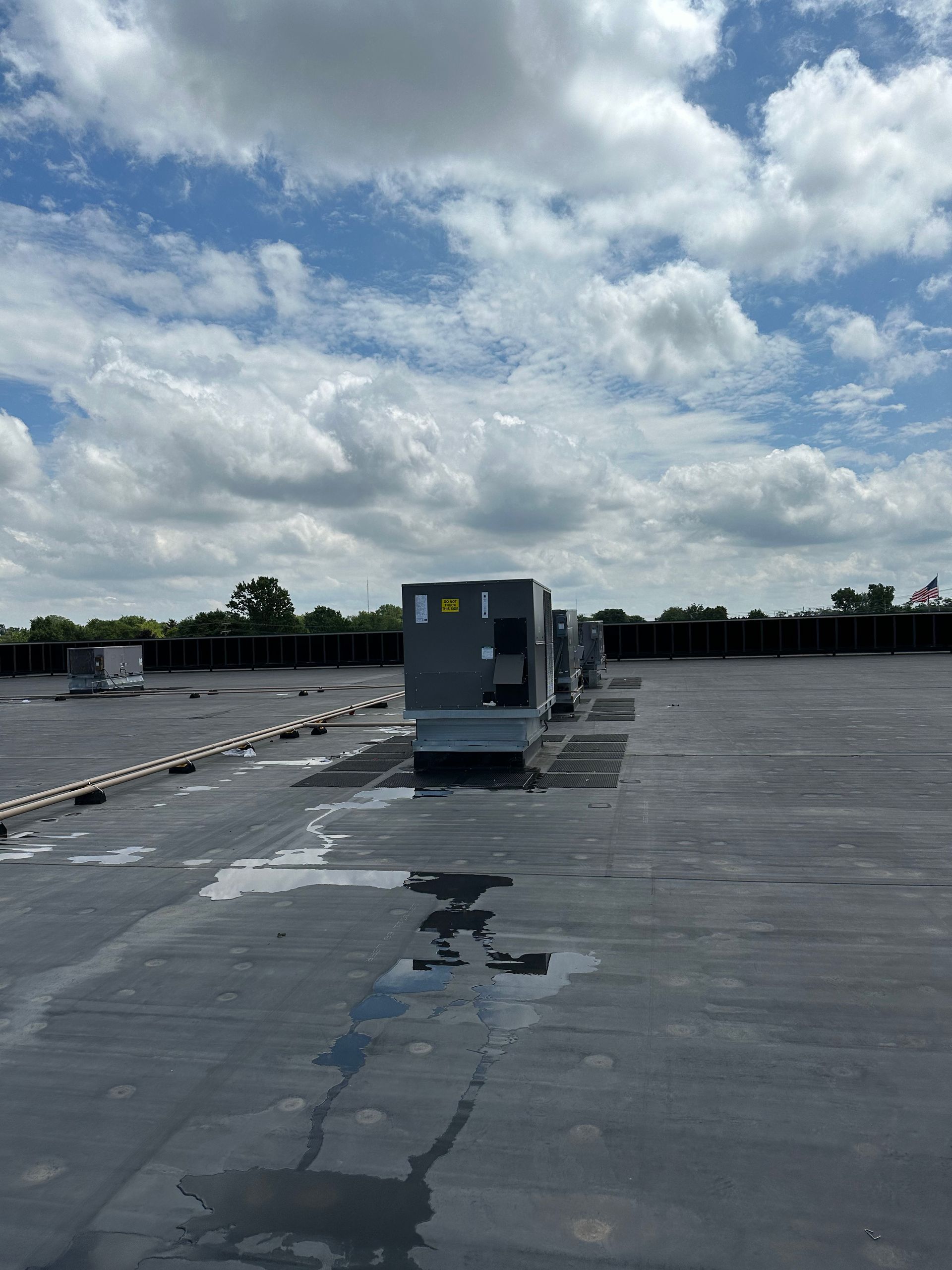 Air conditioning units on a flat rooftop under a cloudy, blue sky.