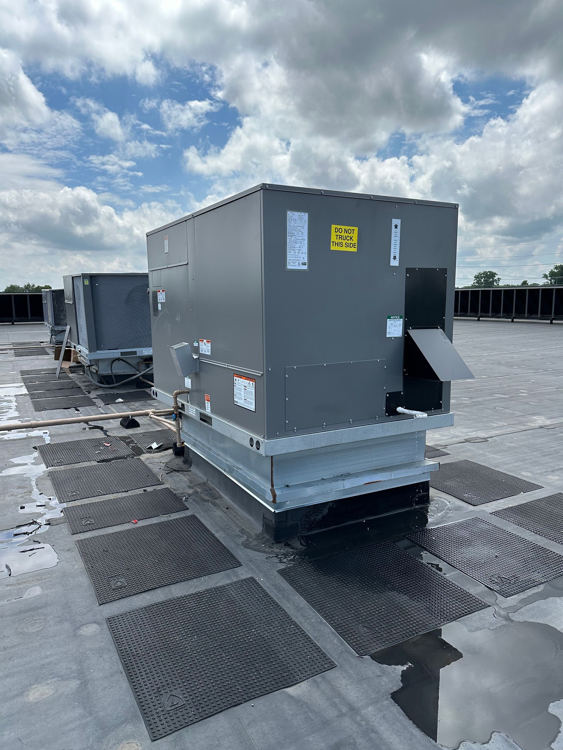 Rooftop air conditioning units on a dark flat roof under a cloudy sky.