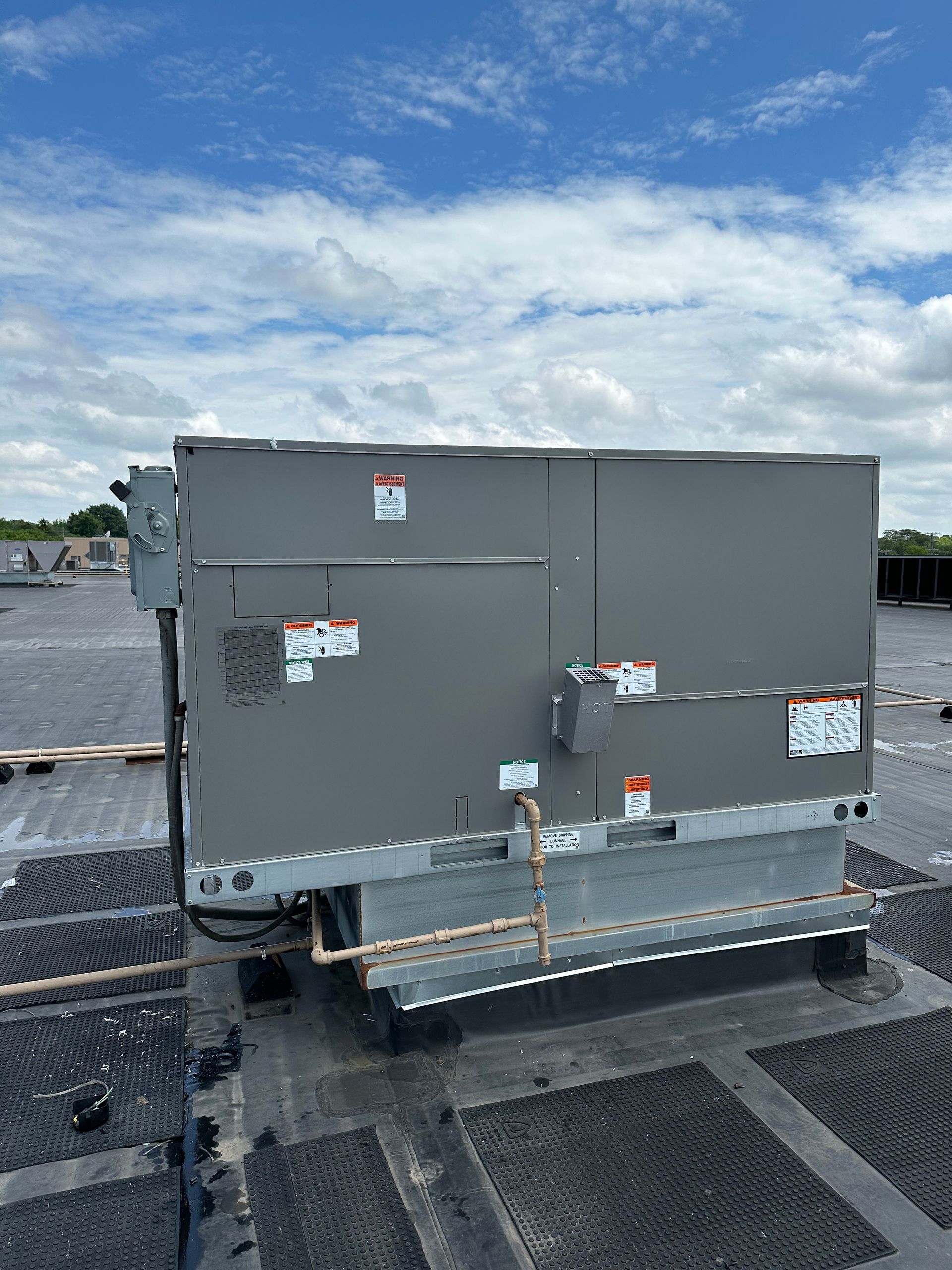 An industrial HVAC unit on a rooftop under a partly cloudy sky.