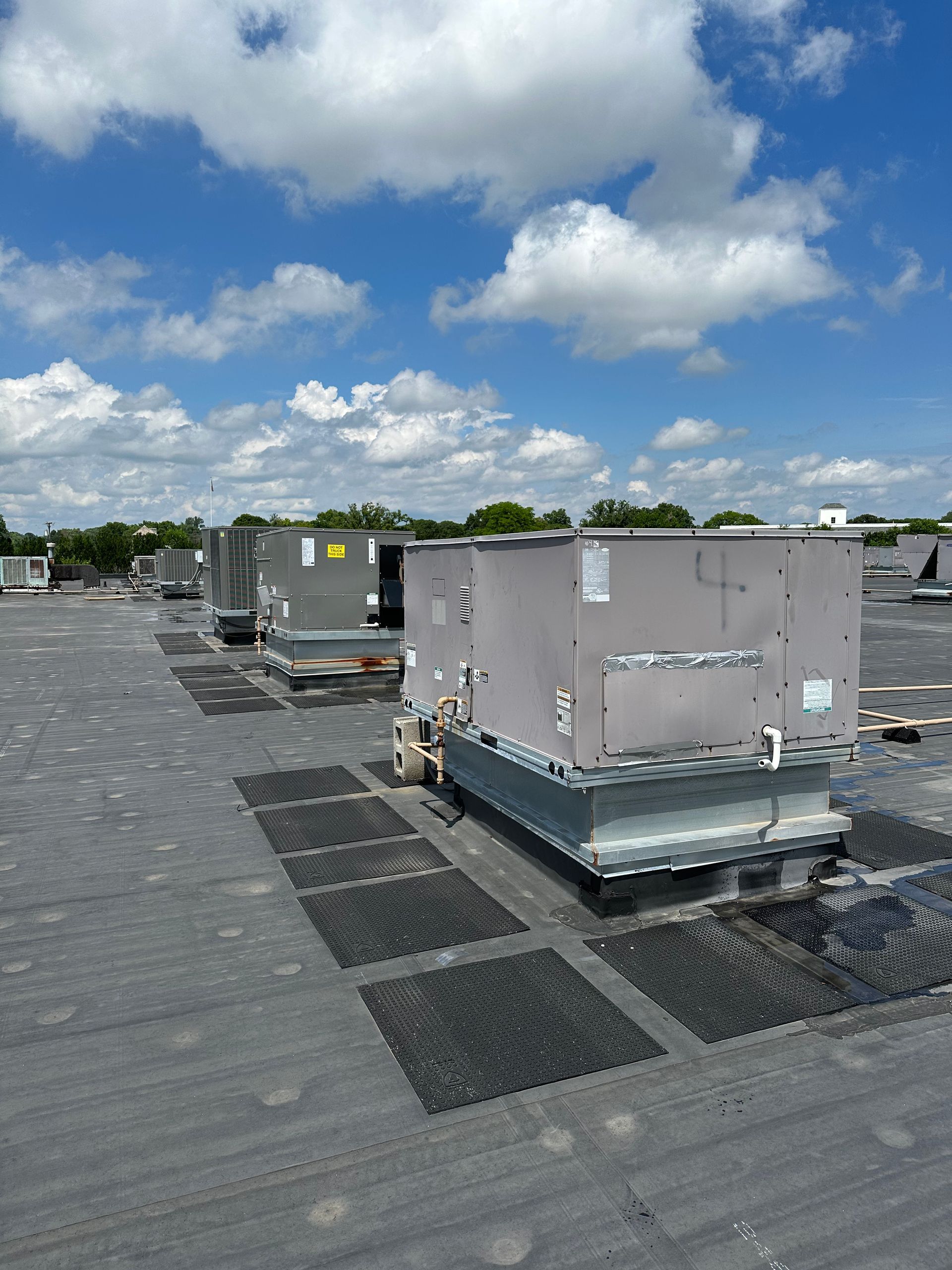 Man inspecting rooftop HVAC unit on a black tar roof. Overcast day.
