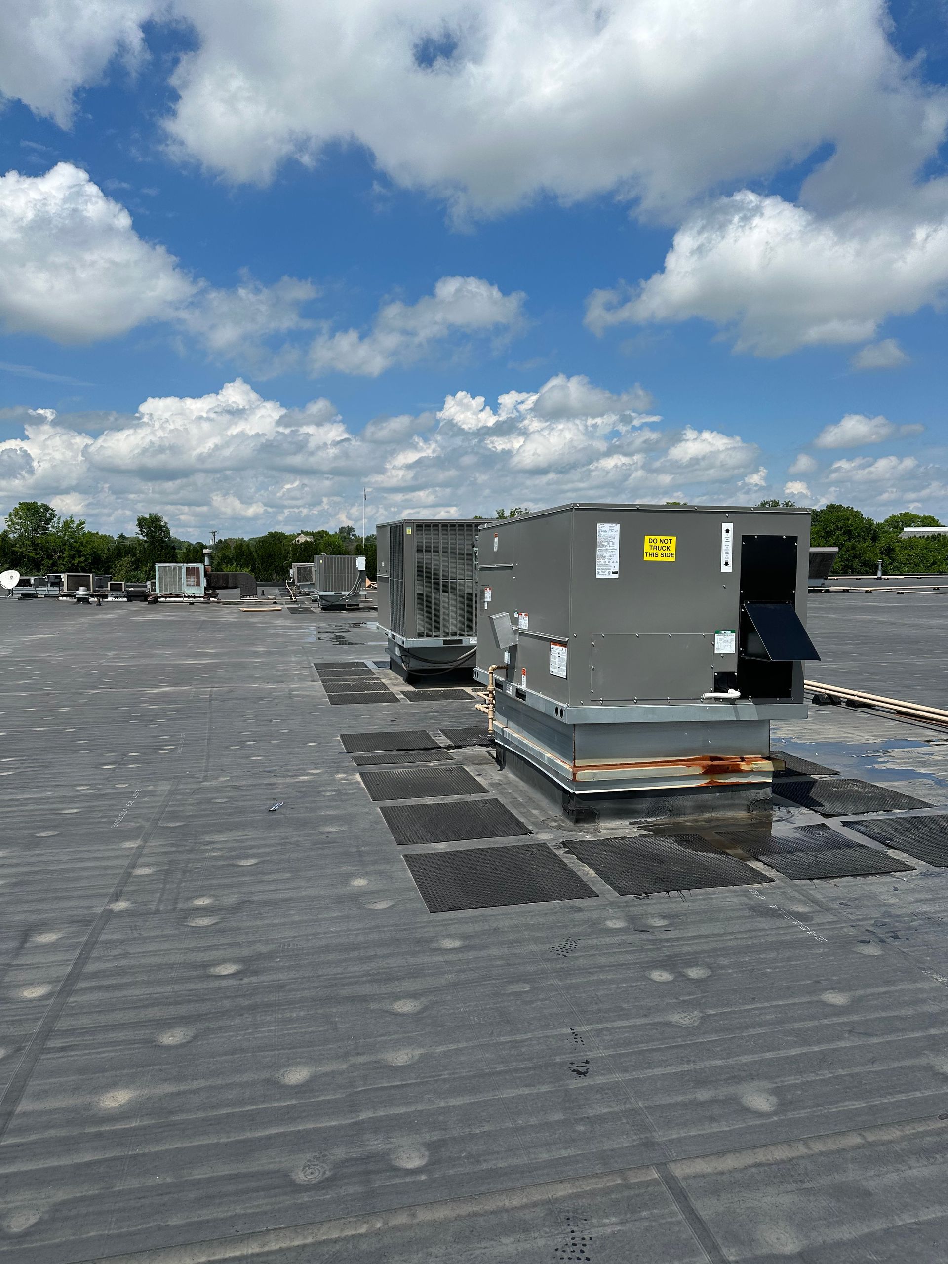 HVAC units on a dark flat roof under a partly cloudy blue sky.