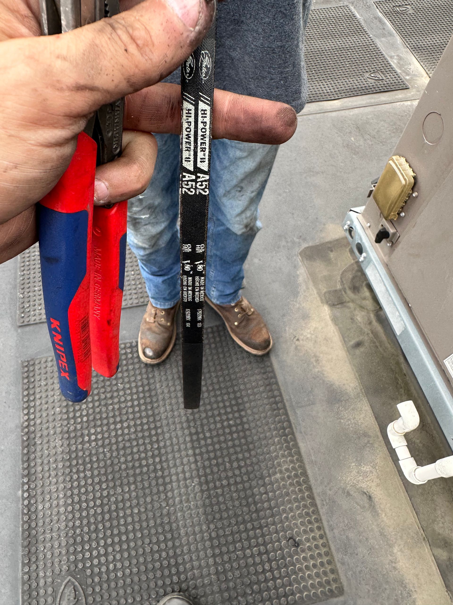 Person holding pliers and a black measurement gauge, standing near an HVAC unit, on a gray surface.