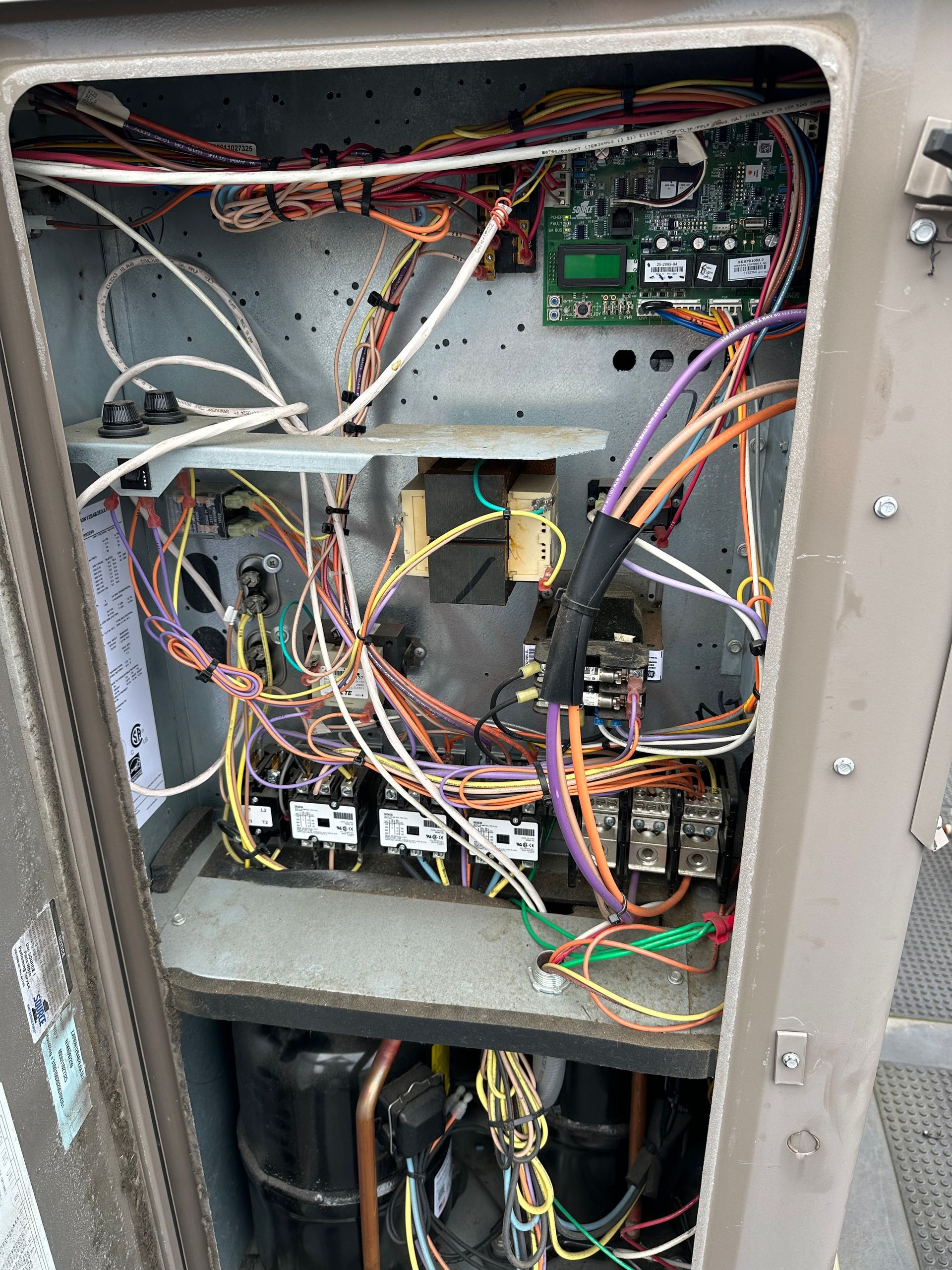 Open electrical panel with wires, circuits, and components, located outdoors.