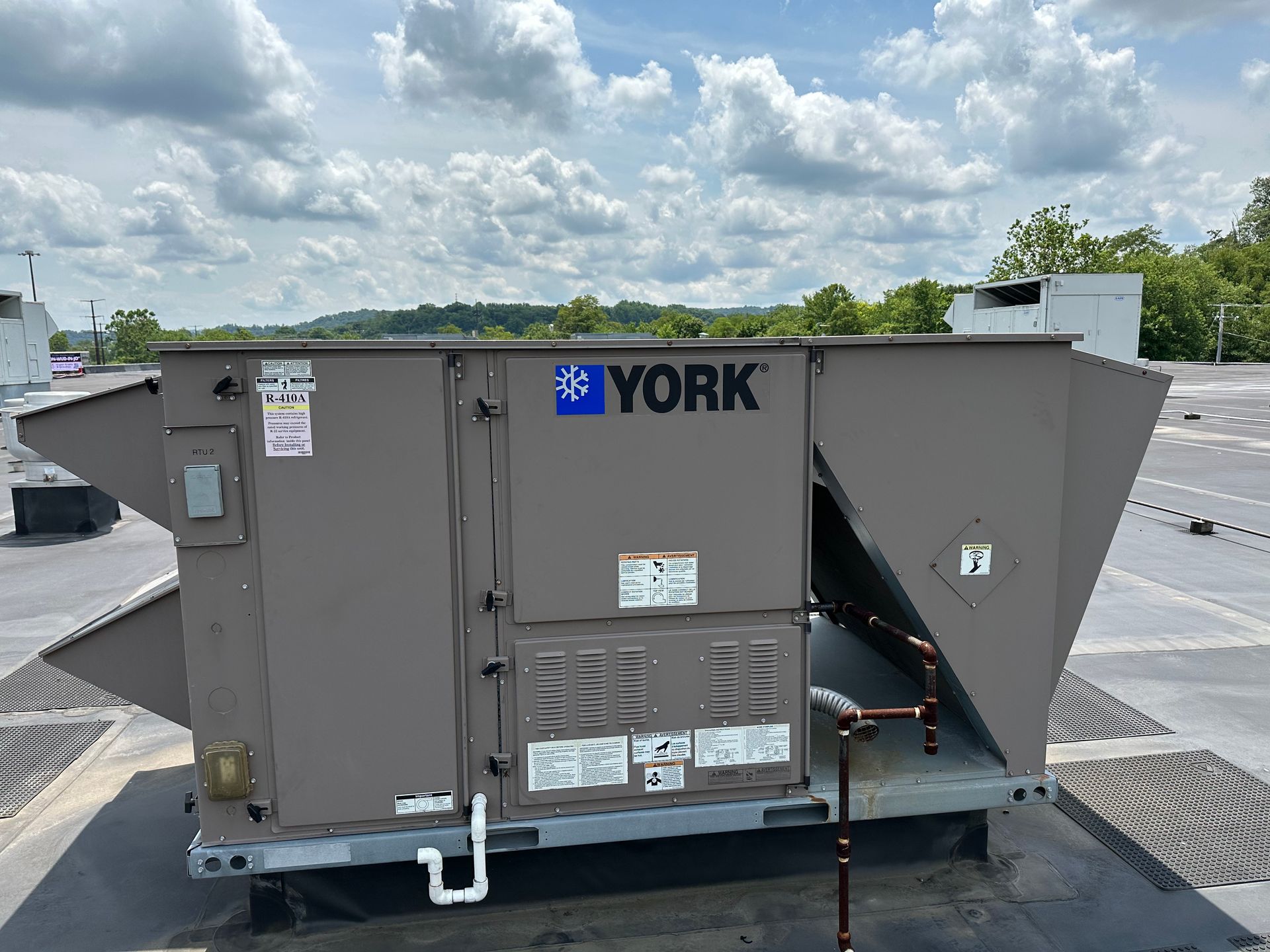 A York rooftop HVAC unit on a flat roof with a cloudy sky backdrop.