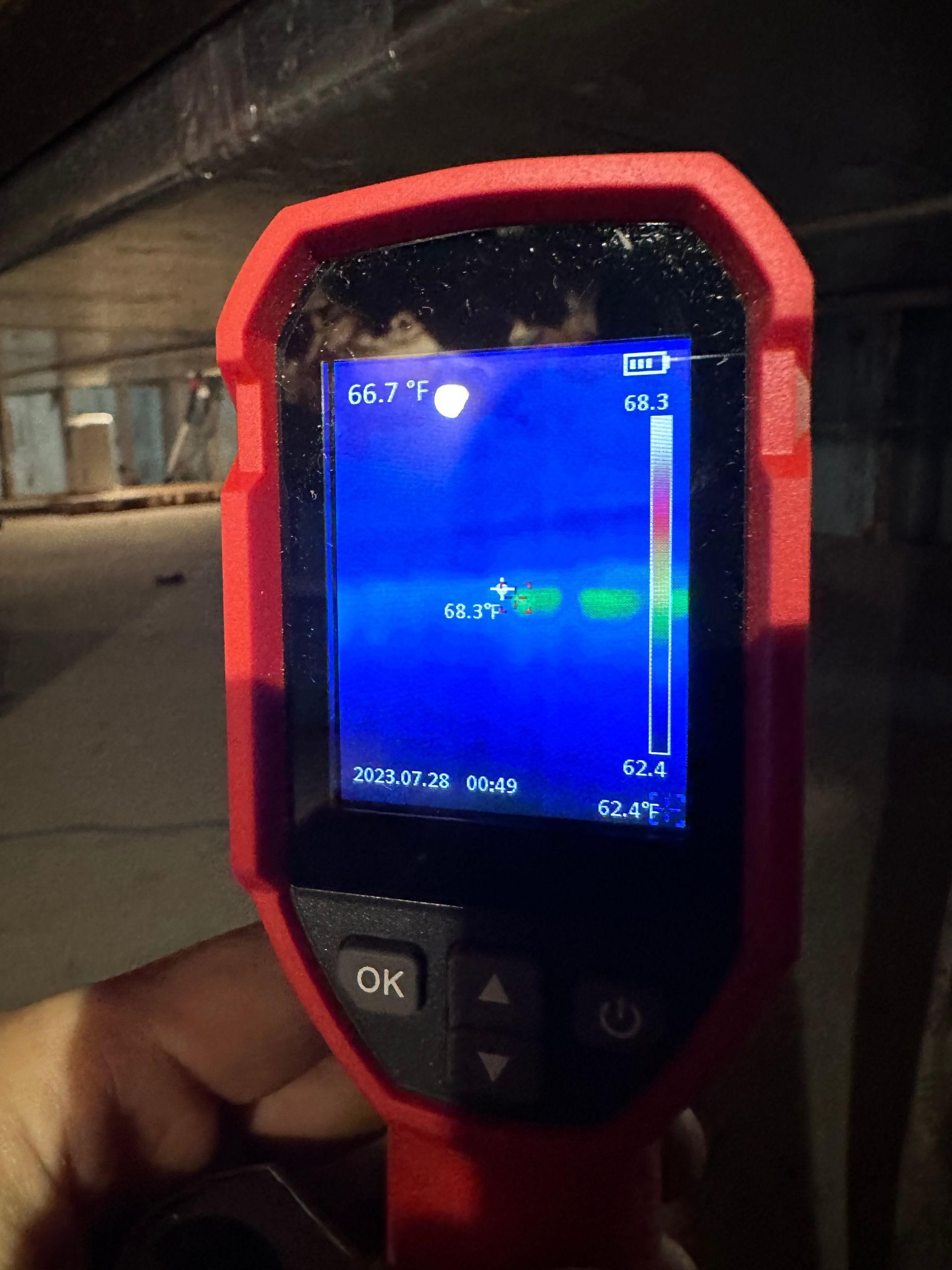 Thermal camera display showing a blue scene with a green spot, likely indicating temperature variation in a crawlspace.