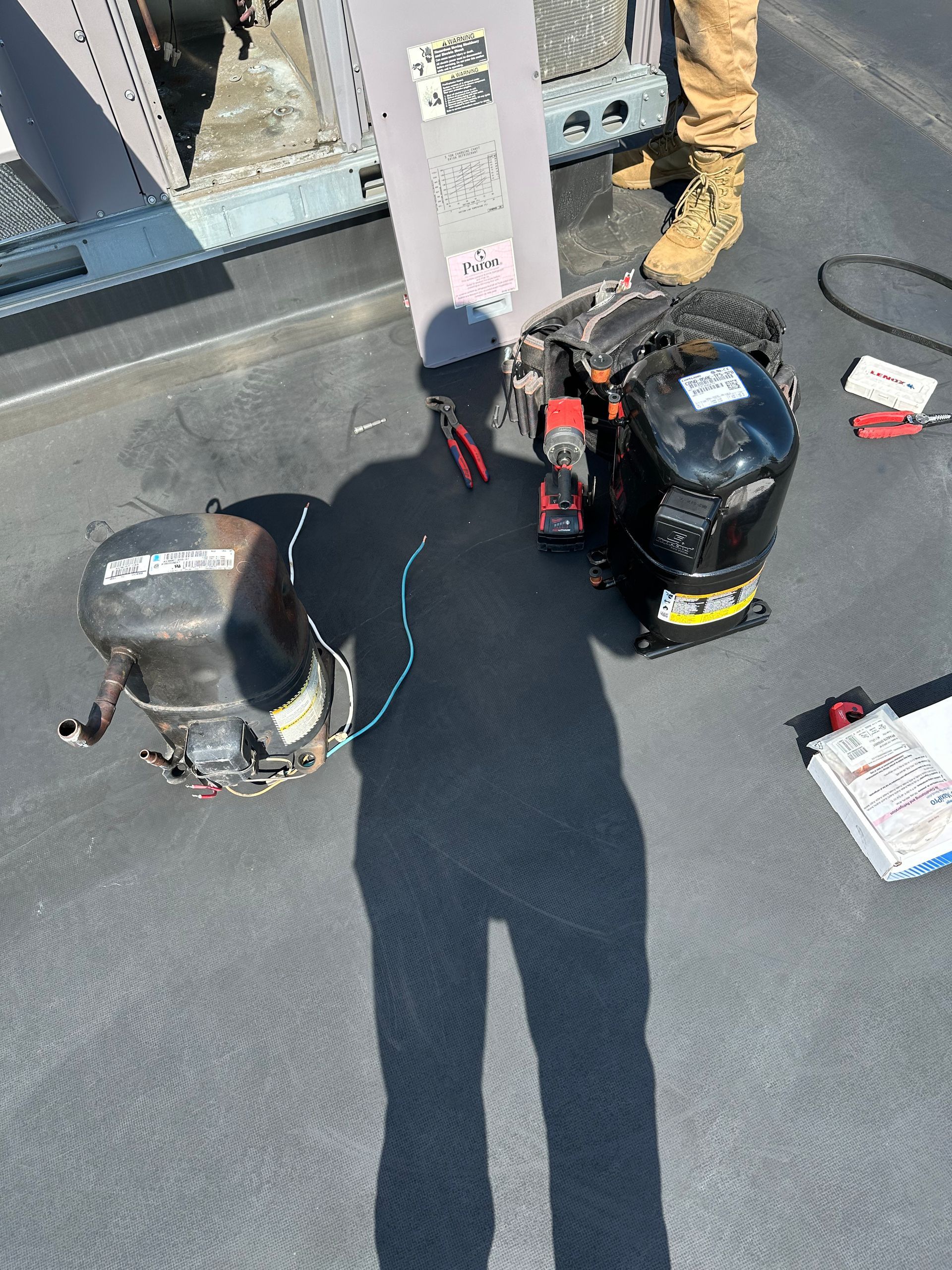 Person holding air conditioning compressors on a rooftop, tools nearby.
